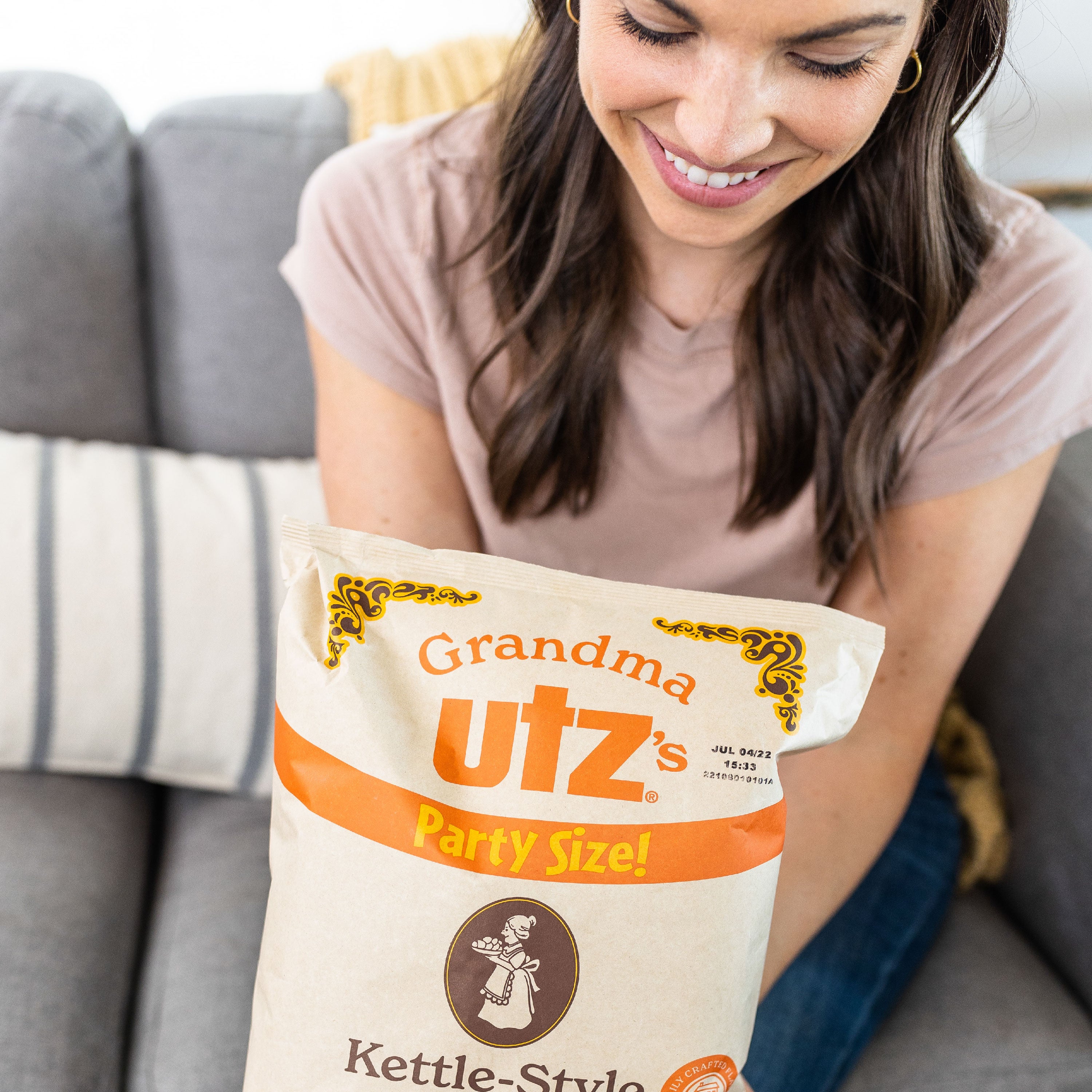 Woman holding a 'Grandma Utz's' kettle-style potato chip bag on a couch.