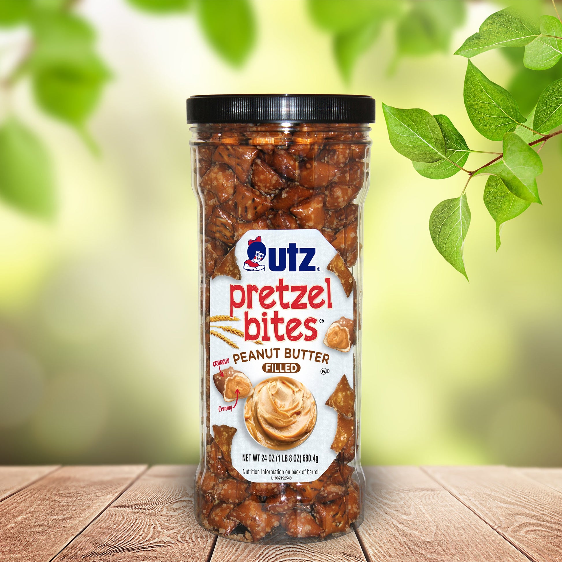 Jar of Utz Pretzel Bites Peanut Butter Filled on a wooden surface with green leaves in the background