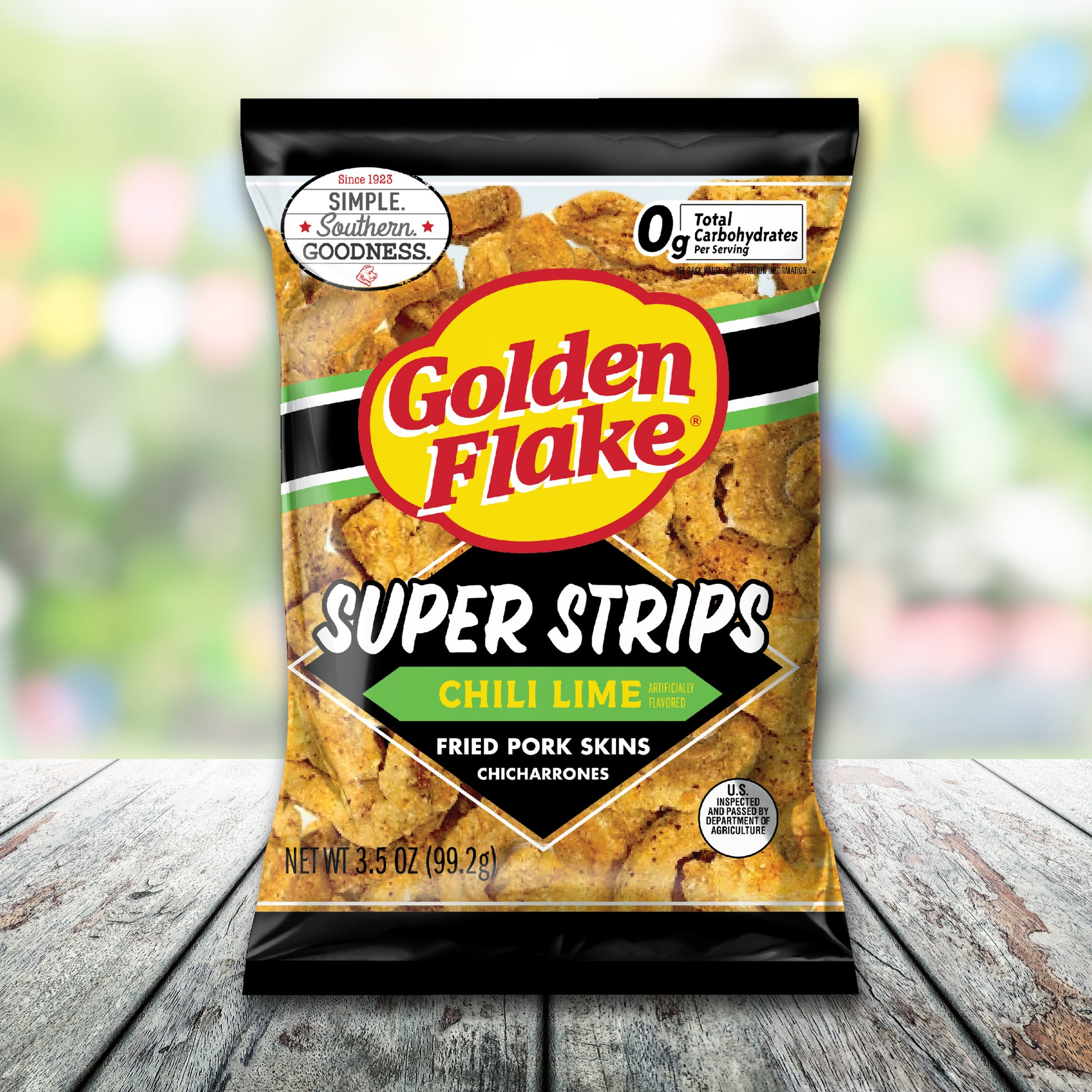 Bag of Golden Flake Super Strips Chili Lime fried pork skins on a wooden surface with a blurred colorful background.