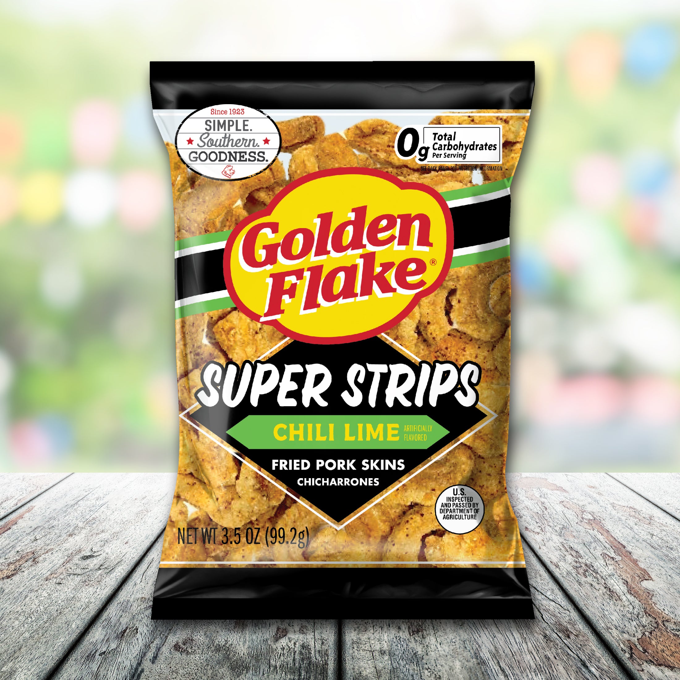 Bag of Golden Flake Super Strips Chili Lime fried pork skins on a wooden surface with a blurred colorful background.
