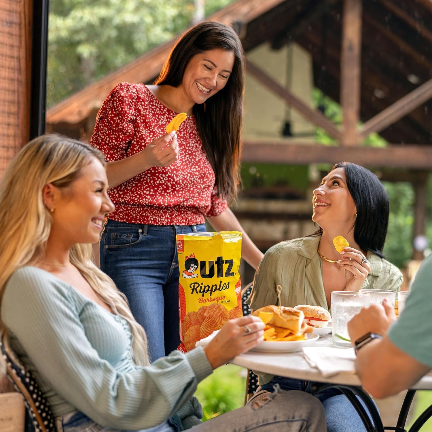 Three women enjoying food outdoors with a box of Utz Rippled chips.