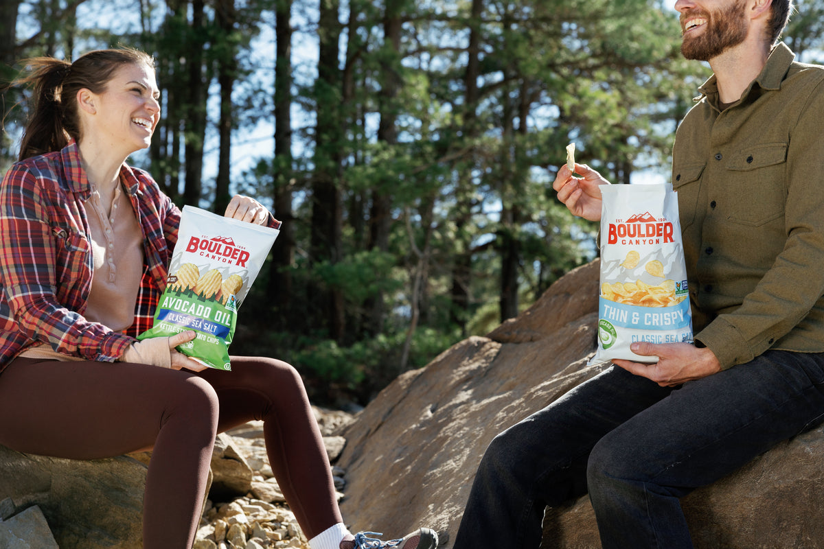 Two people sitting outdoors with Boulder Canyon chips