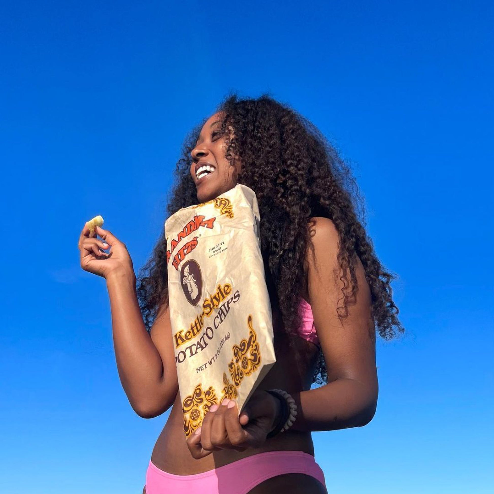 Woman holding a bag of kettle-style potato chips against a blue sky