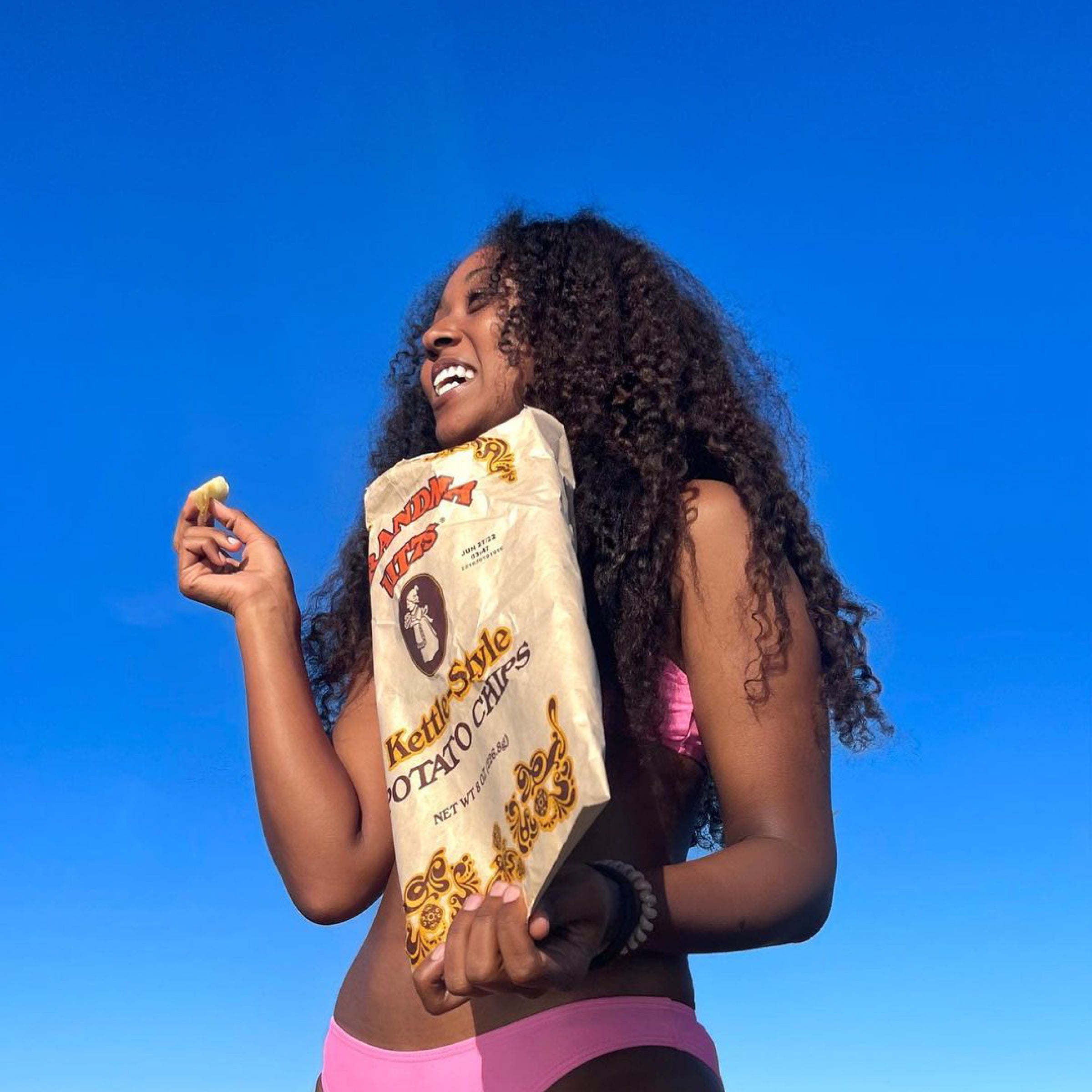 Woman holding a bag of kettle-style potato chips against a blue sky