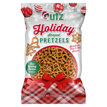 Front of the Utz Holiday Shaped Pretzels 14oz bag. Features the Utz logo, product name, and an image of pretzels shaped like snowflakes, trees, and bells. Includes festive holiday graphics with red ornaments and white pine branches. Highlights 'Fun Holiday Recipes on Back' and net weight of 14 oz (396.9g).