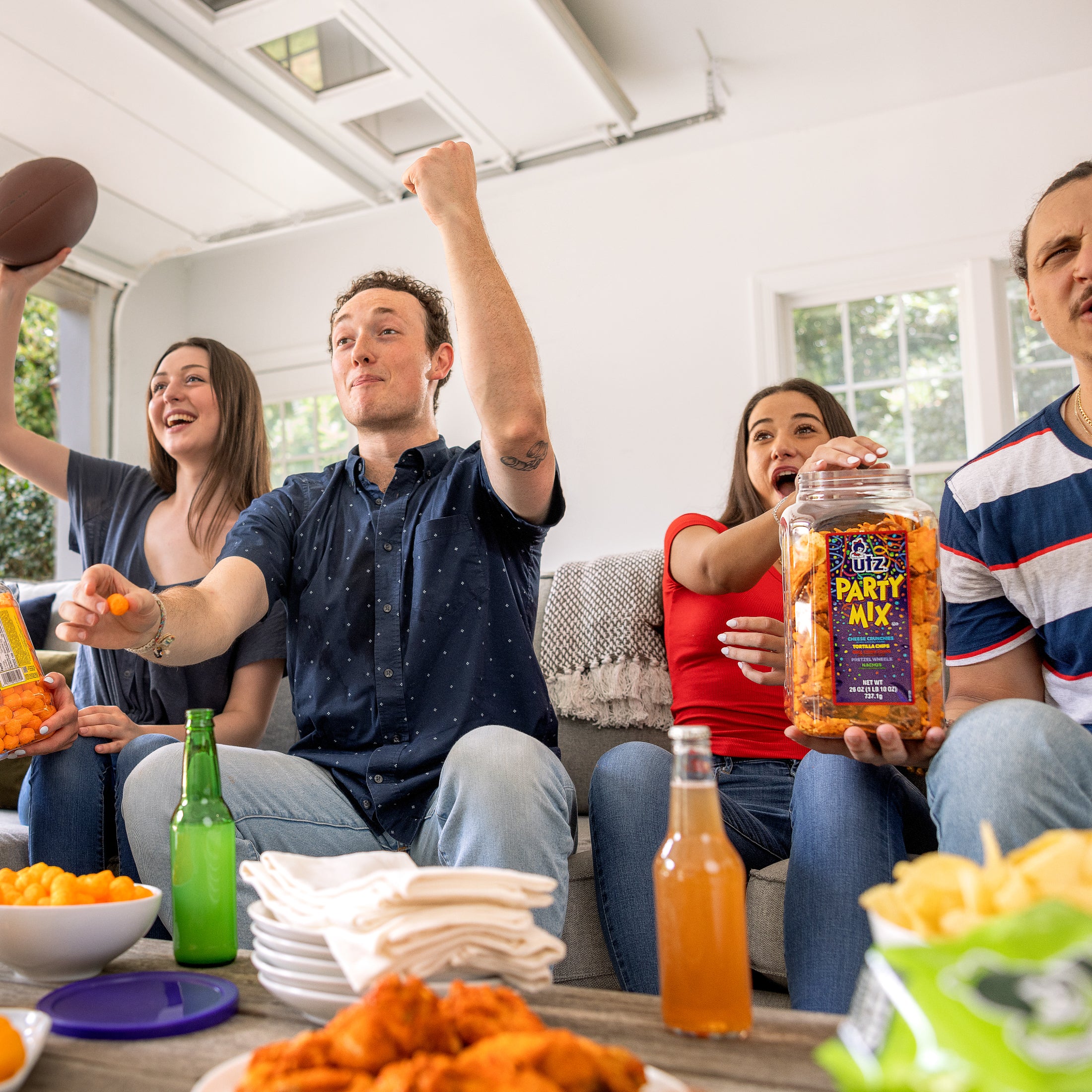 Group of people enjoying a party with snacks and drinks, including a jar of Party Mix.