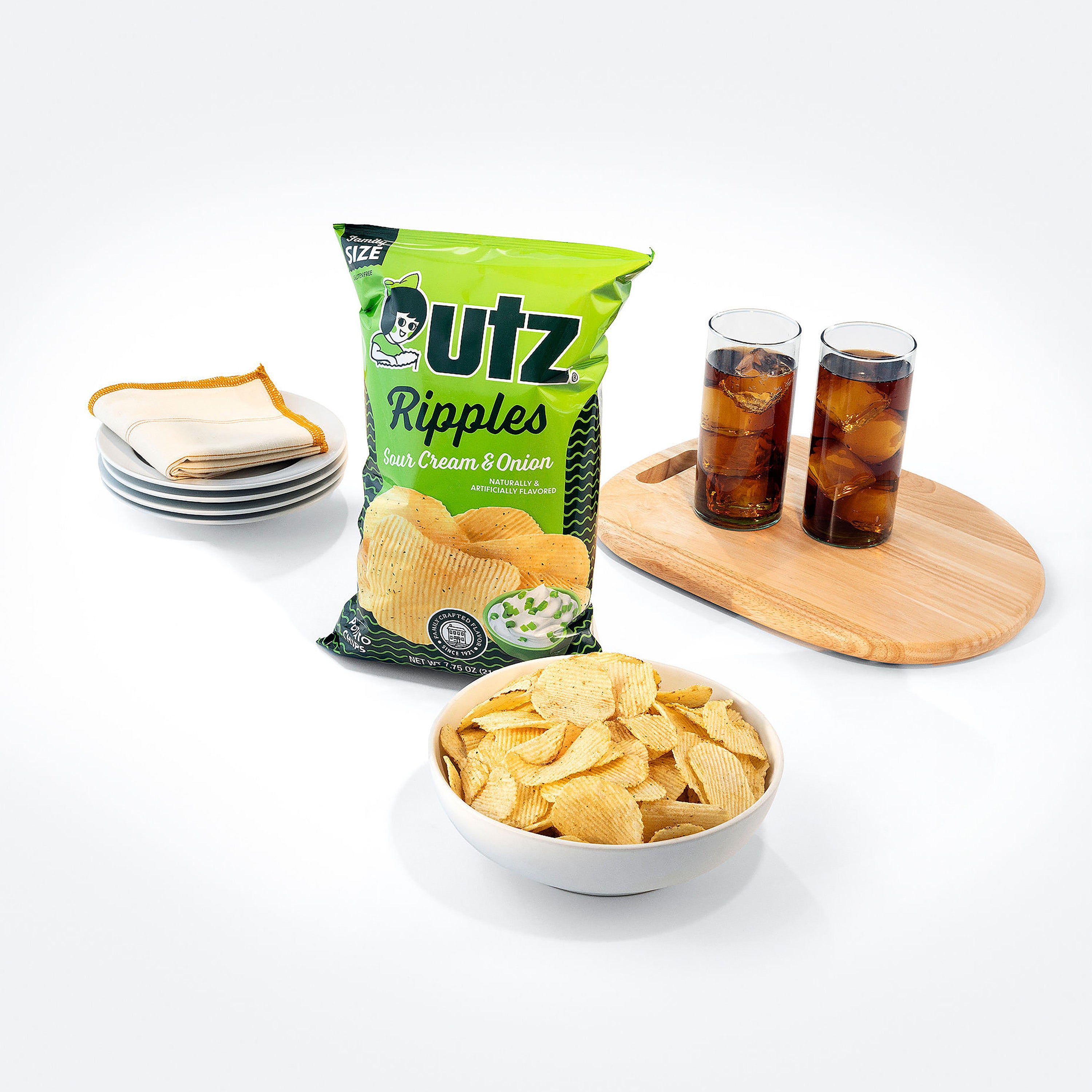 Utz Ripples Sour Cream & Onion chips with a bowl of chips, a bag of chips, and two glasses of soda on a white background.