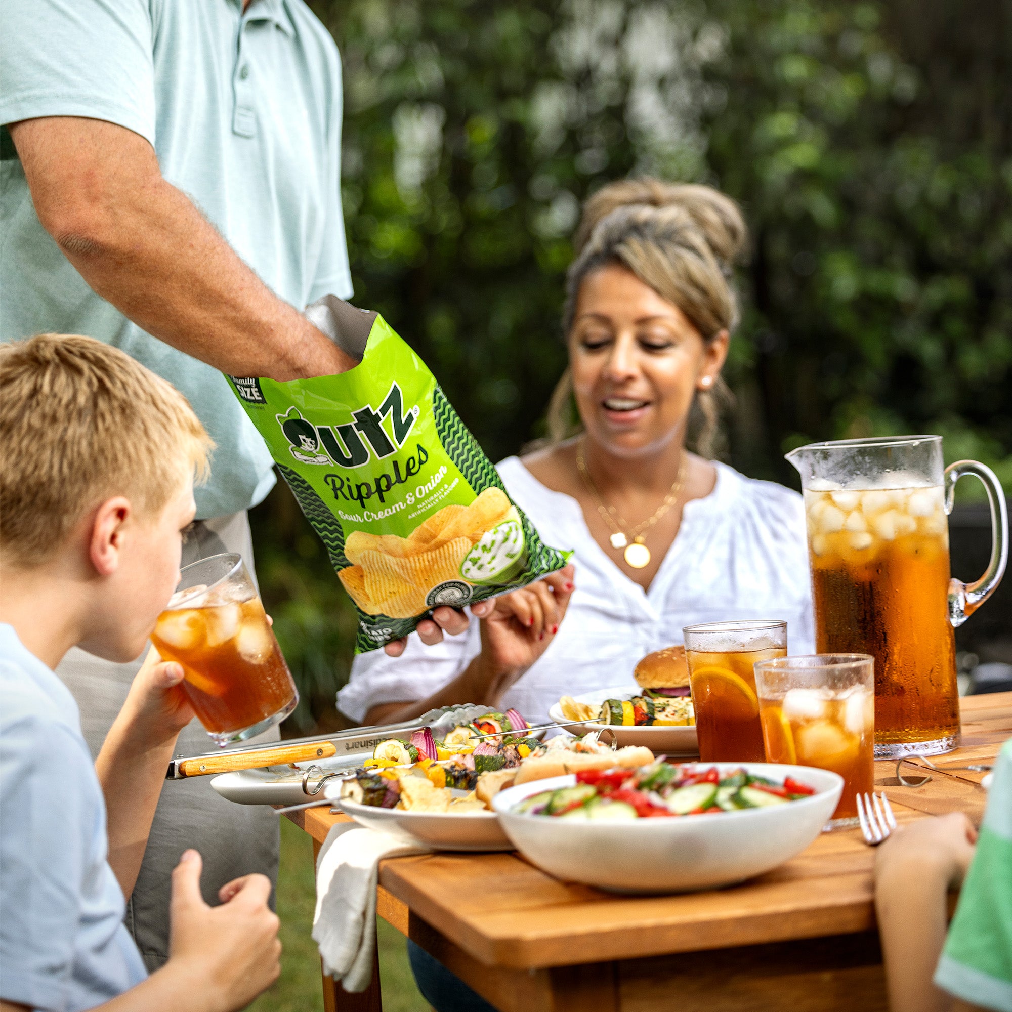 Family at a picnic table with a person holding a bag of utz Rippled potato chips.