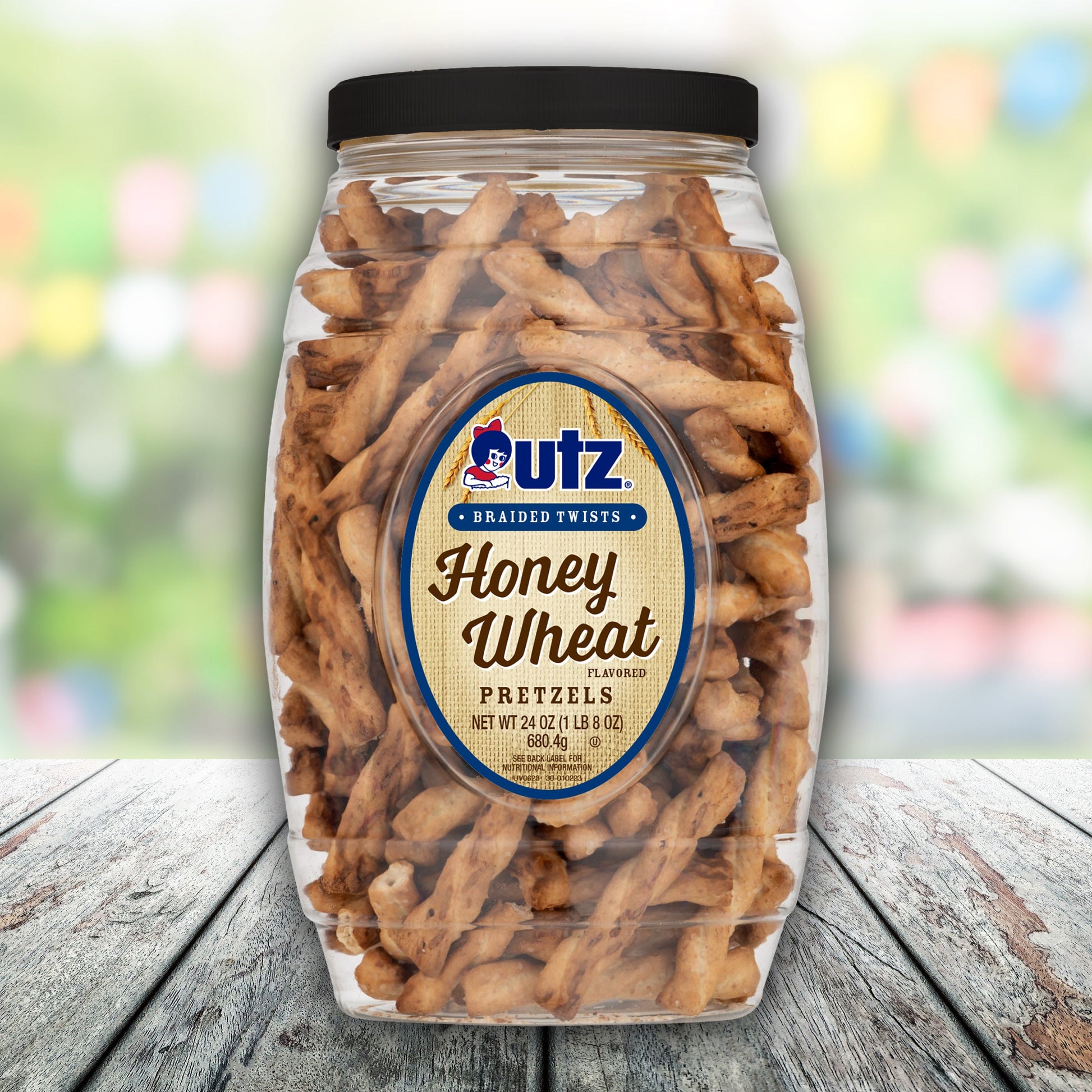 Jar of Utz Honey Wheat Pretzel Twists on a wooden surface with a blurred colorful background