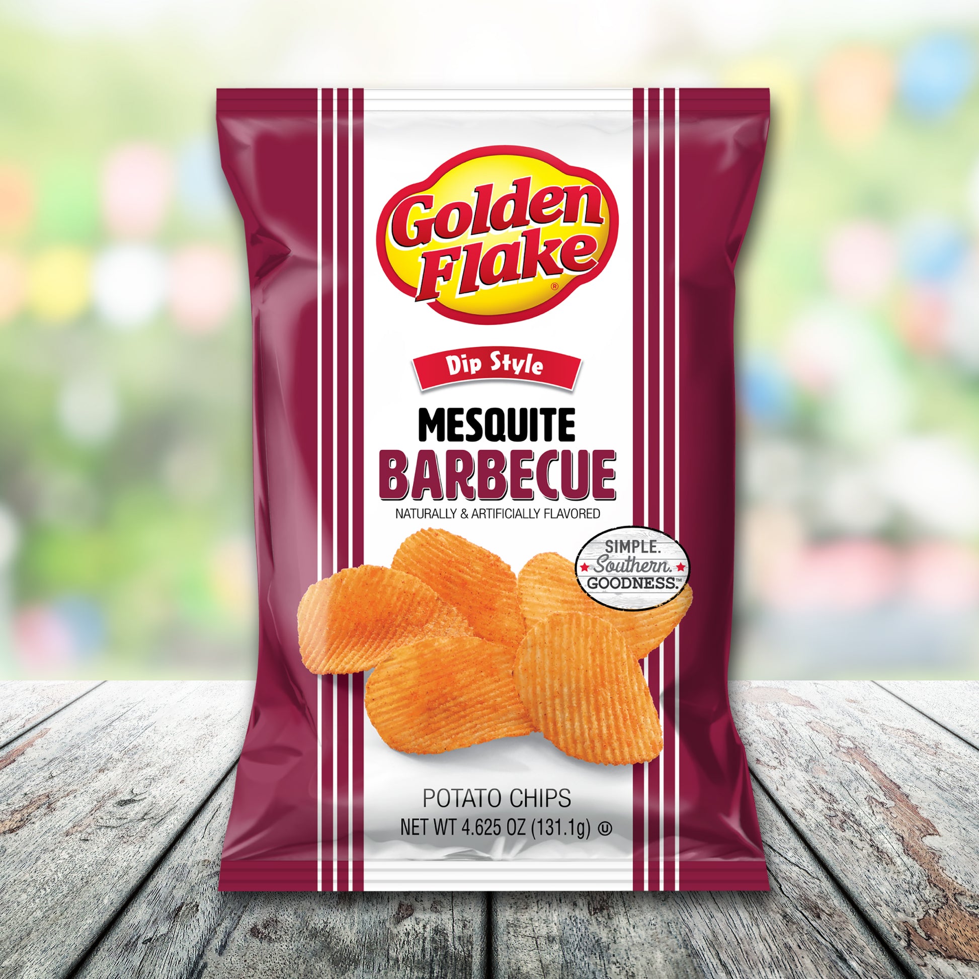 Packaging of Golden Flake Mesquite Barbecue potato chips on a wooden surface with a blurred colorful background.