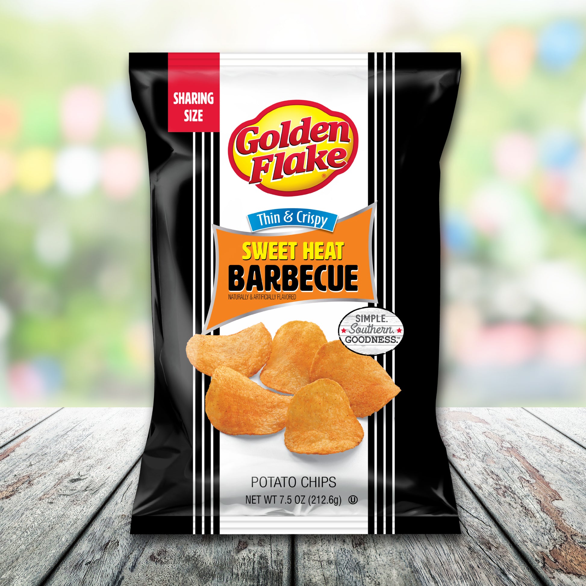 Bag of Golden Flake Sweet Heat Barbecue potato chips on a wooden surface with a blurred colorful background