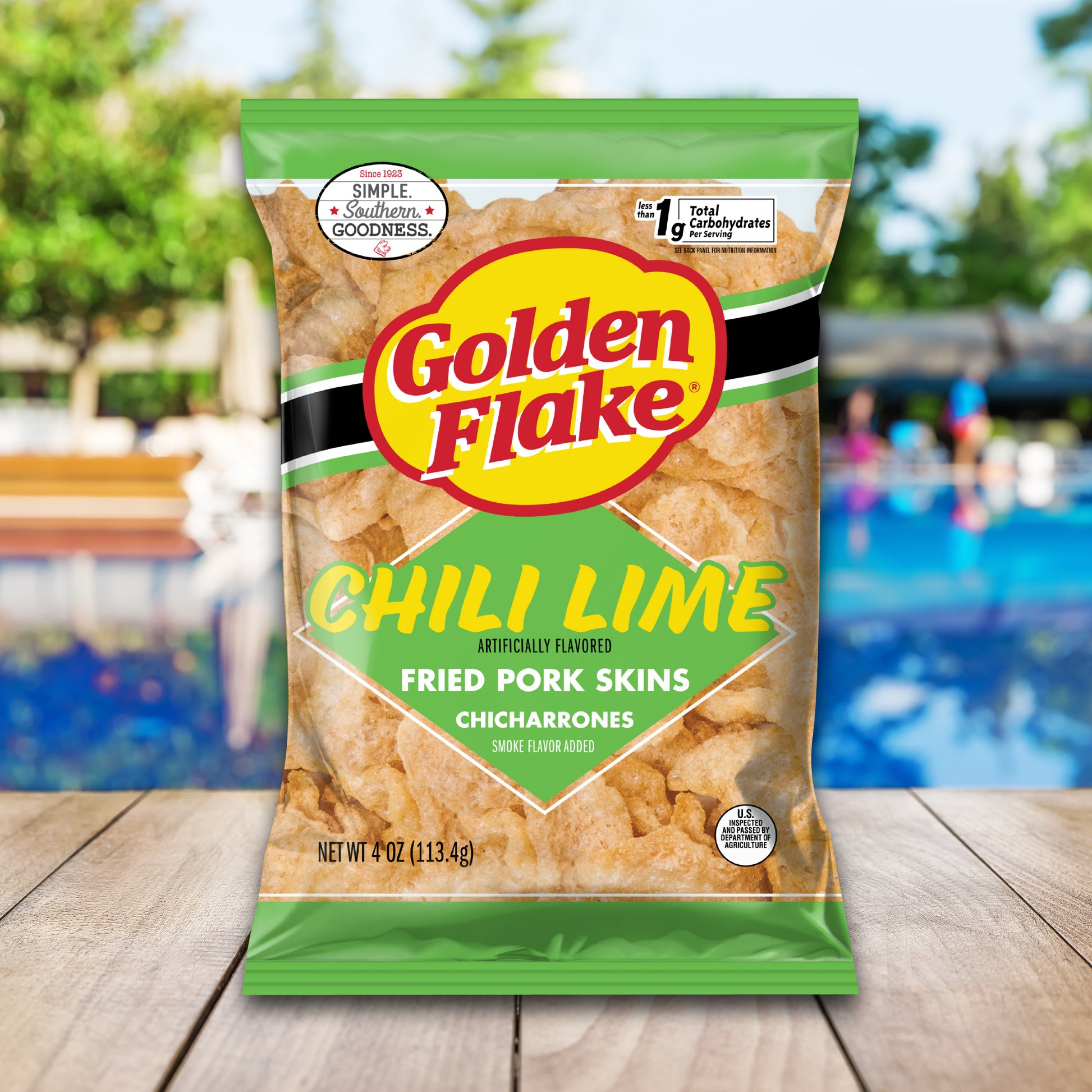 Bag of Golden Flake Chili Lime fried pork skins on a wooden surface with a blurred outdoor background.