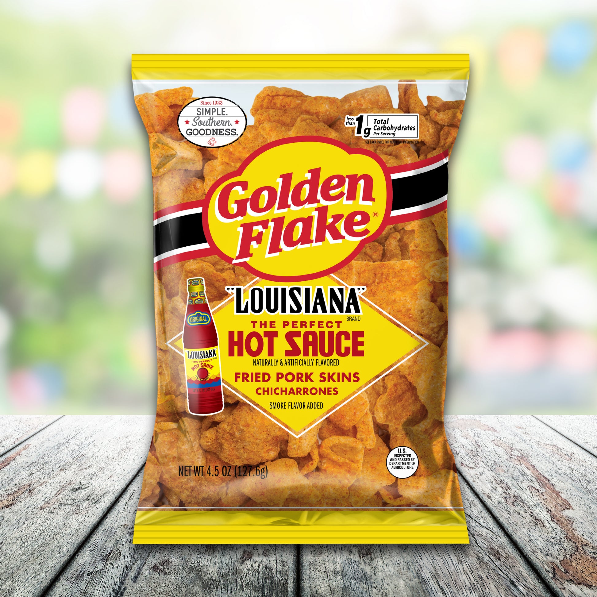 Packaging of Golden Flake Louisiana Fried Pork Skins with hot sauce on a wooden surface.
