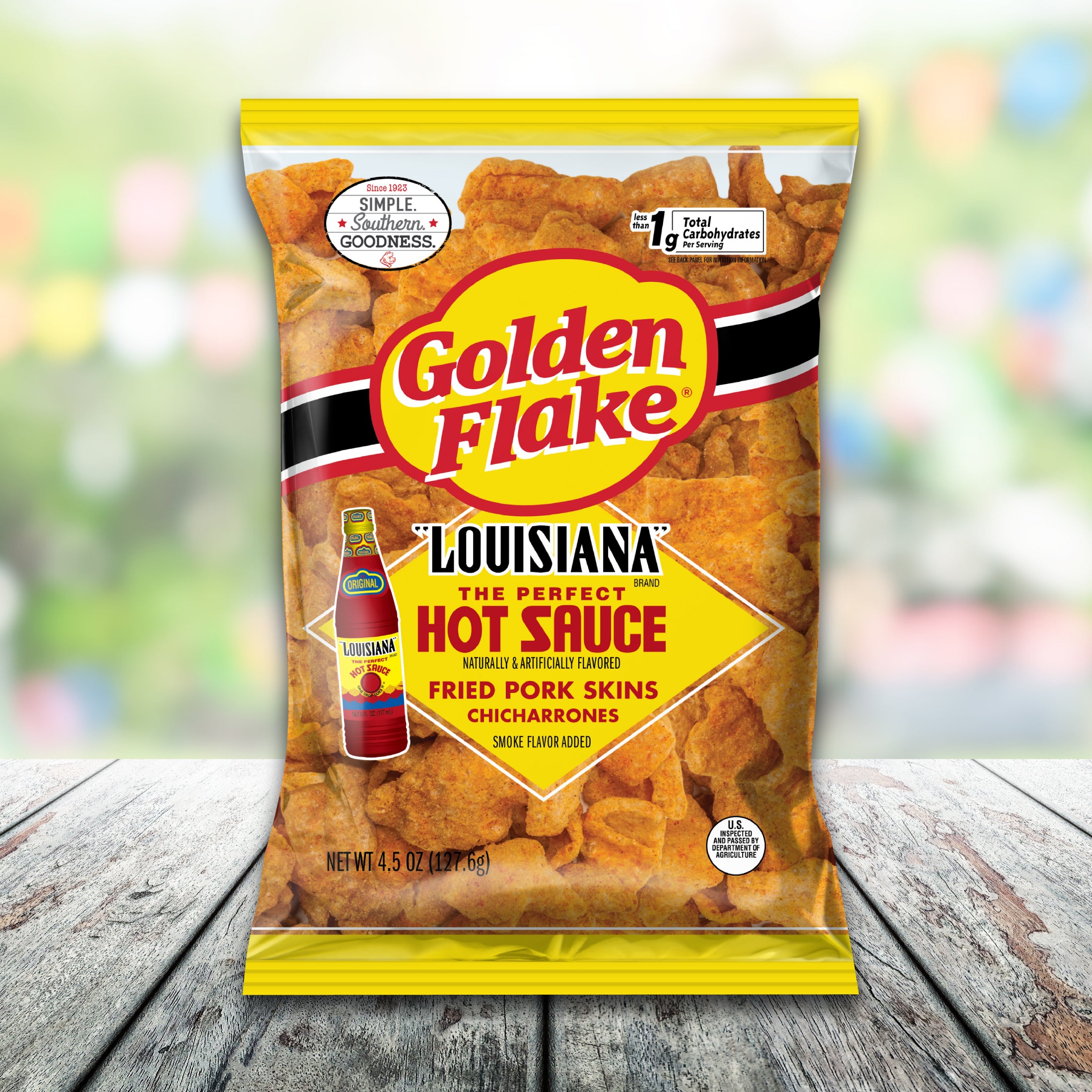 Packaging of Golden Flake Louisiana Fried Pork Skins with hot sauce on a wooden surface.