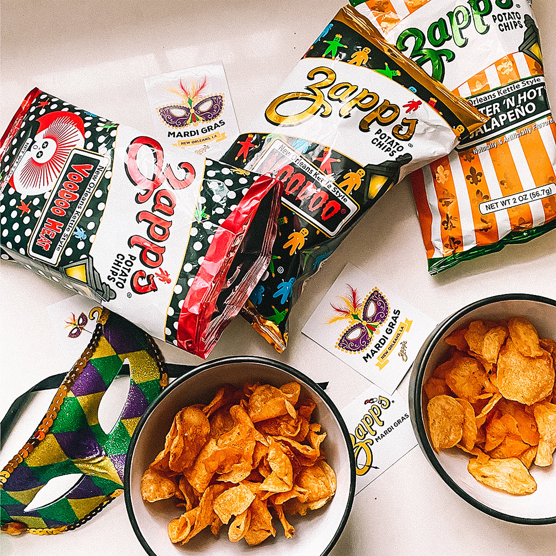 Zapp's potato chips in various flavors with packaging and bowls of chips on a white surface.