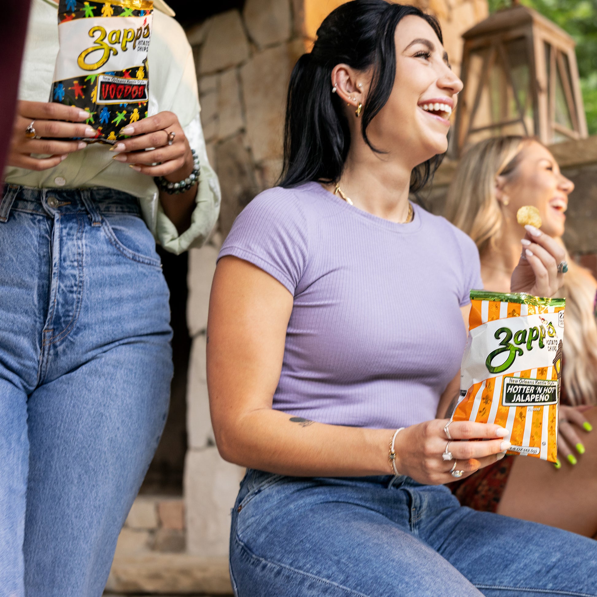 Woman holding a Zapps hot sauce packet outdoors with another person in the background.