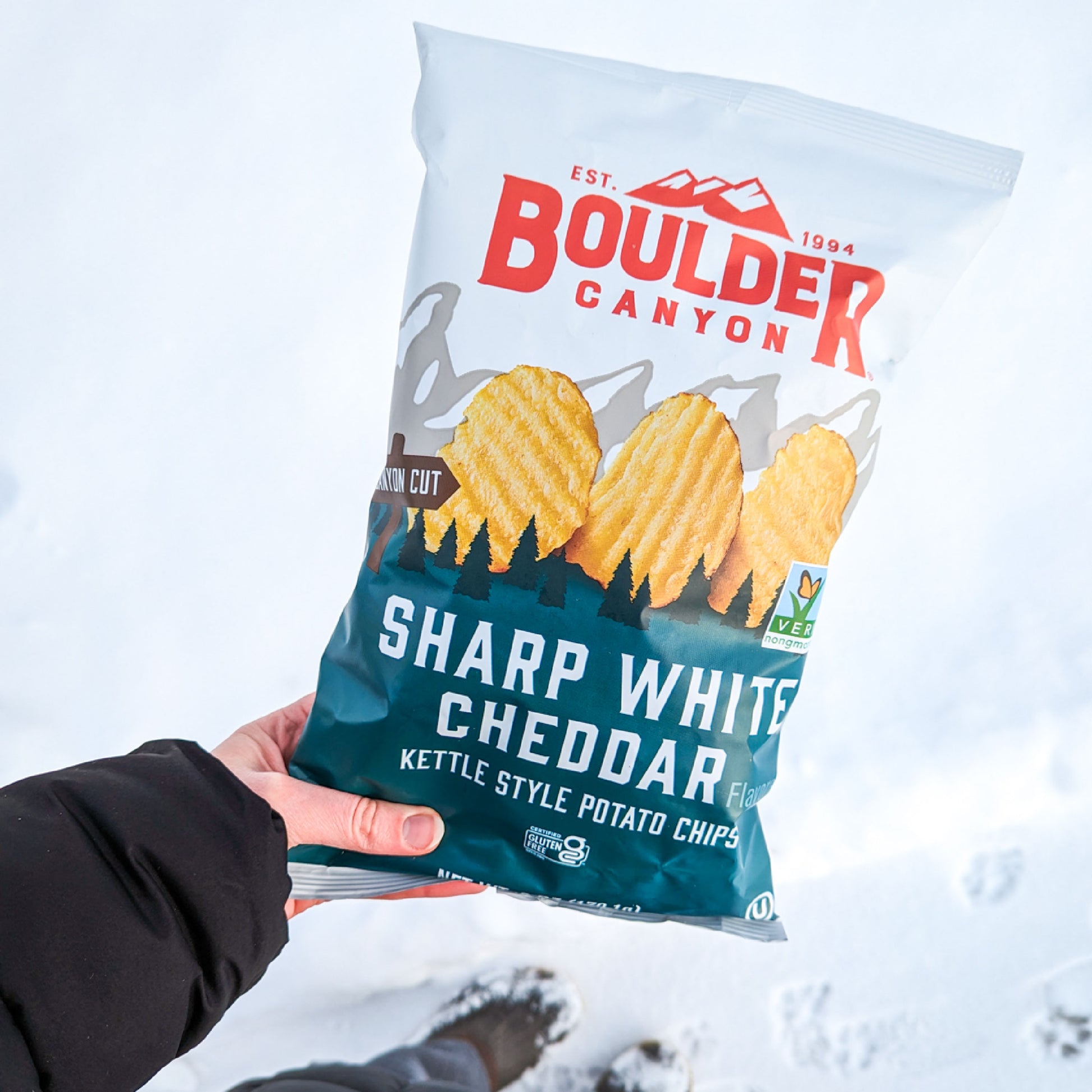 Boulder Canyon Sharp White Cheddar potato chips bag held in snow