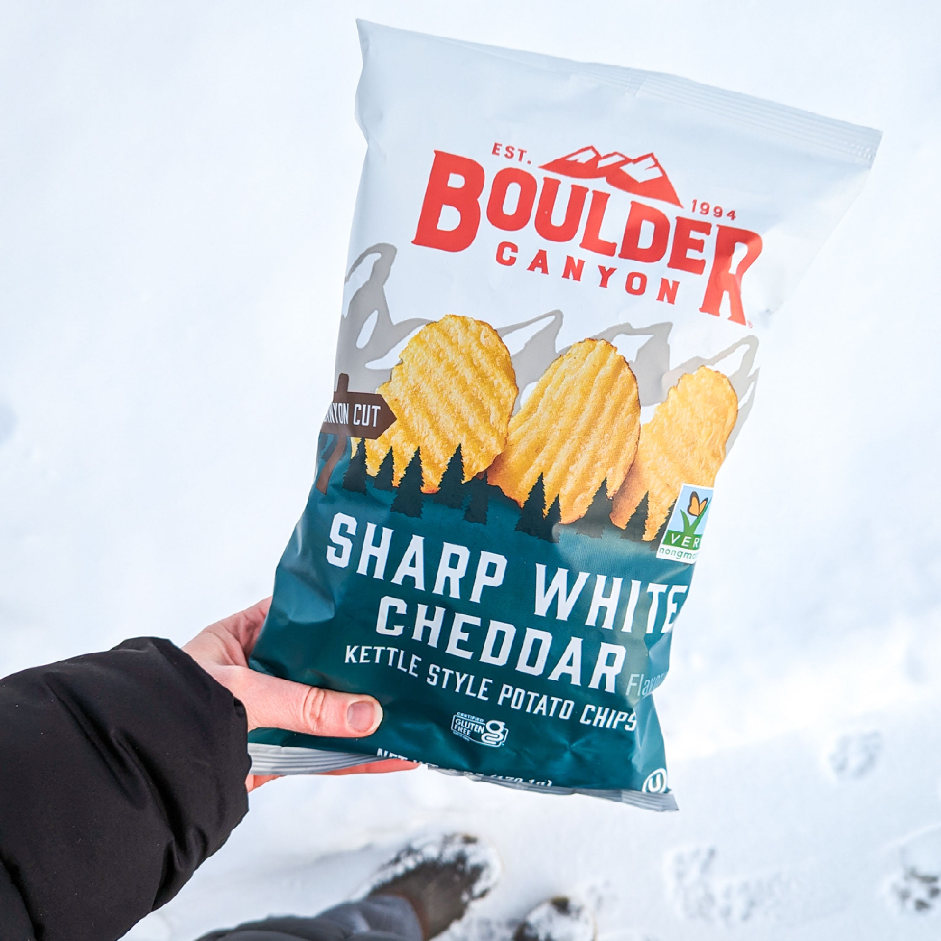 Boulder Canyon Sharp White Cheddar potato chips bag held in snow
