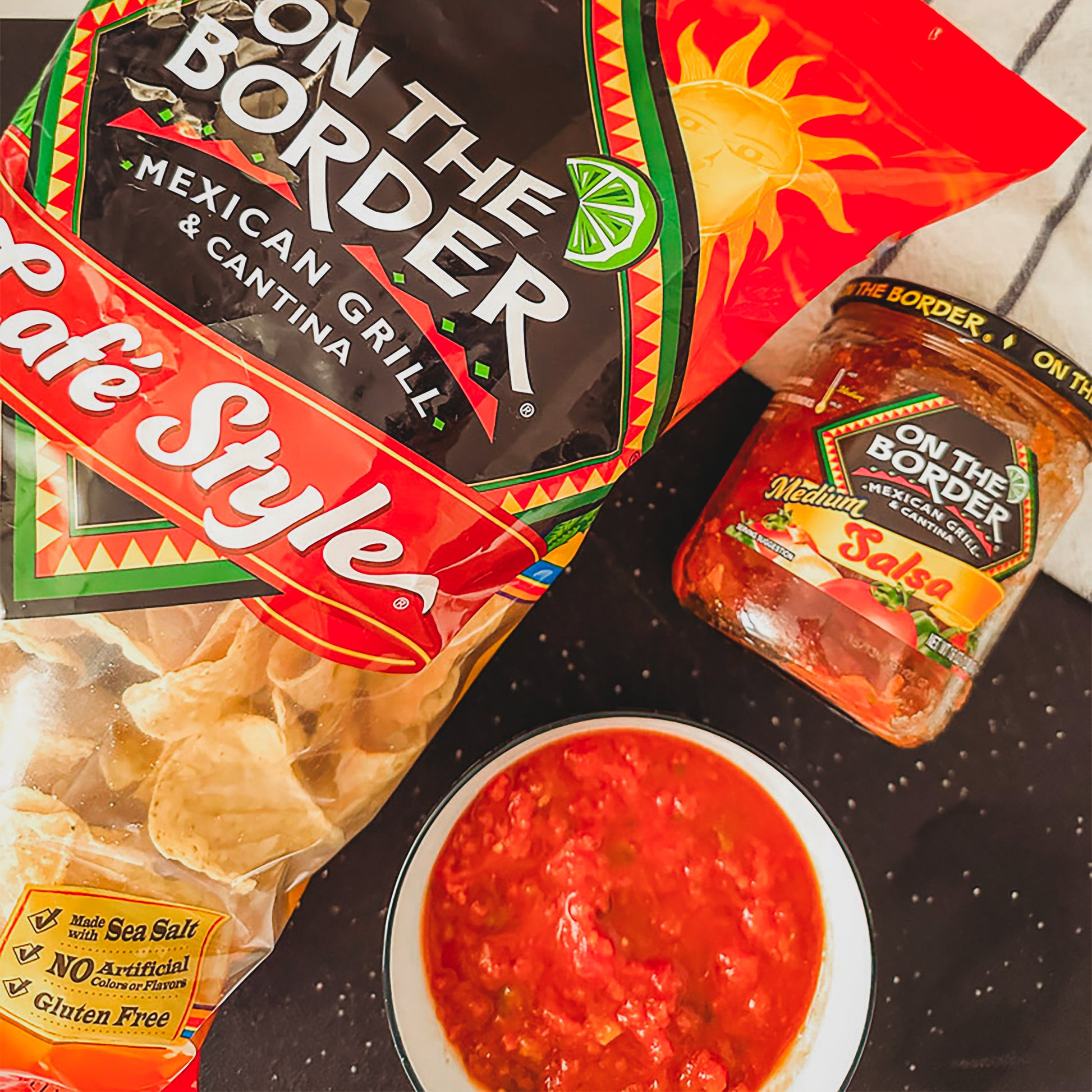 On The Border Mexican Grill & Cantina products including tortilla chips, salsa, and a bag of chips on a black surface.