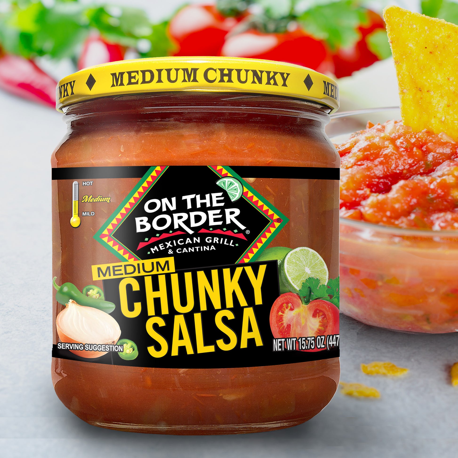 Jar of On The Border Medium Chunky Salsa with a bowl of salsa and tortilla chips in the background.