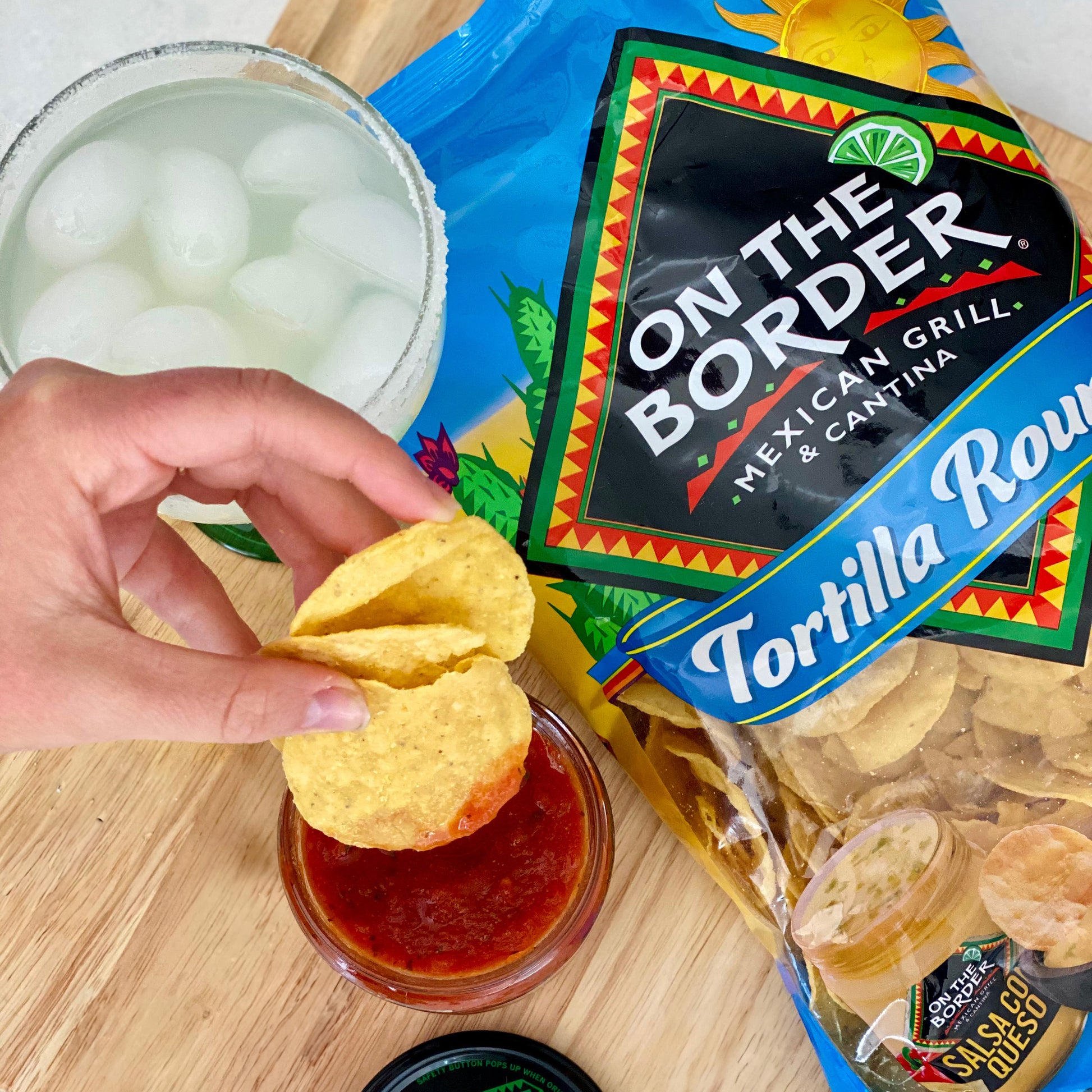 Person dipping a tortilla chip into salsa with 'On The Border' packaging in the background.