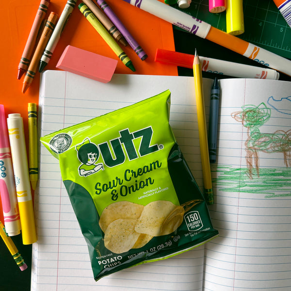 Outz Sour Cream & Onion potato chips packet on a desk with school supplies