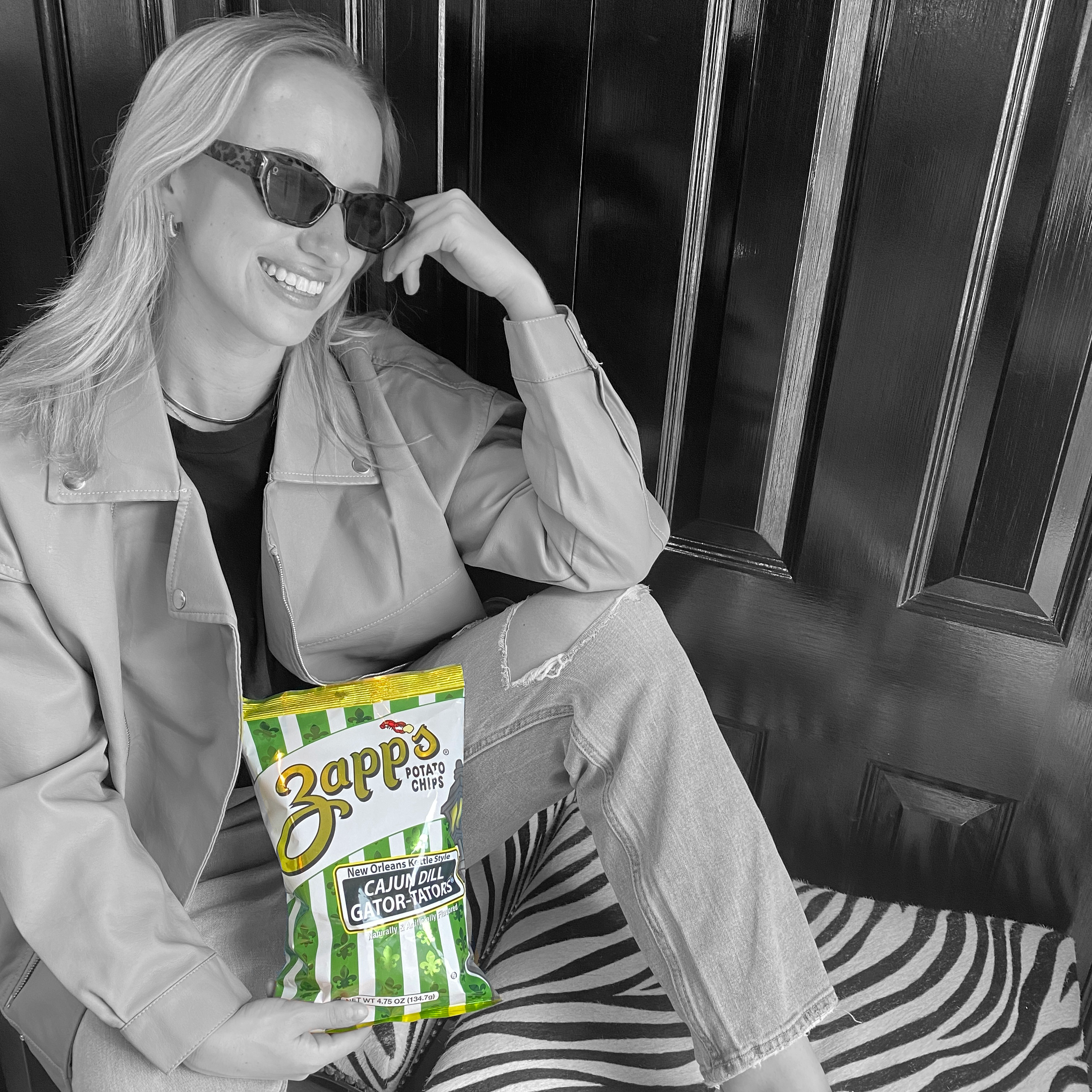 Woman holding a Zapp's potato chip bag in front of a black door.