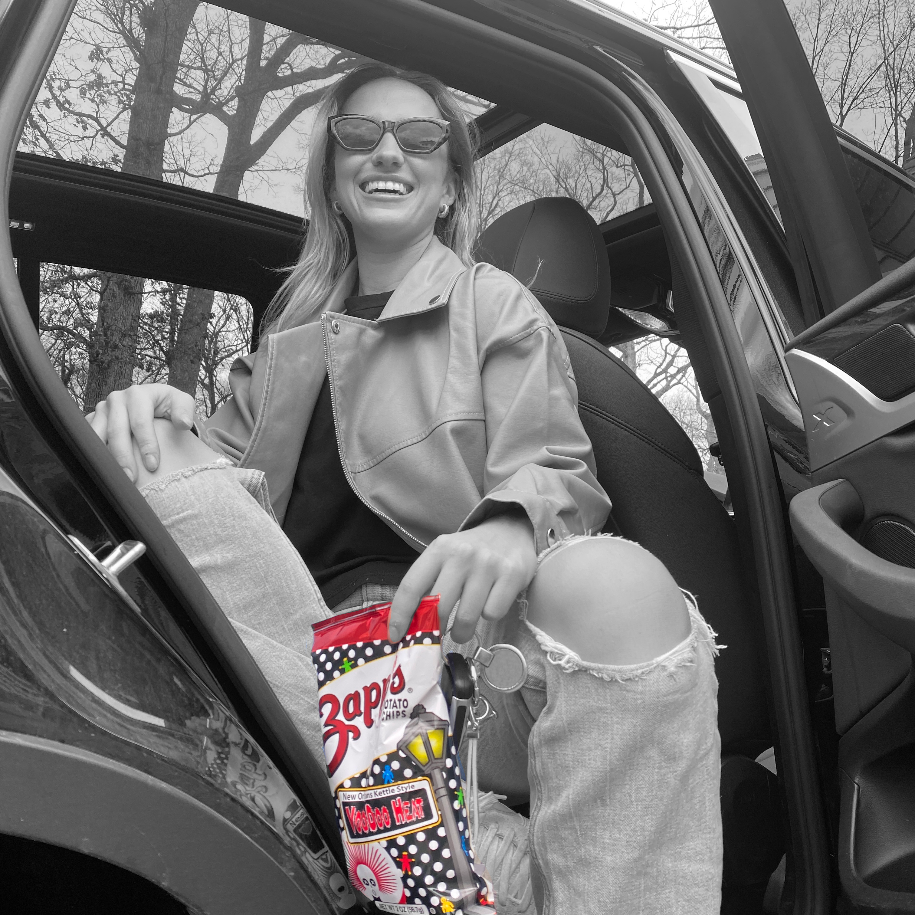 Woman sitting in a car holding a bag of candy, wearing sunglasses.