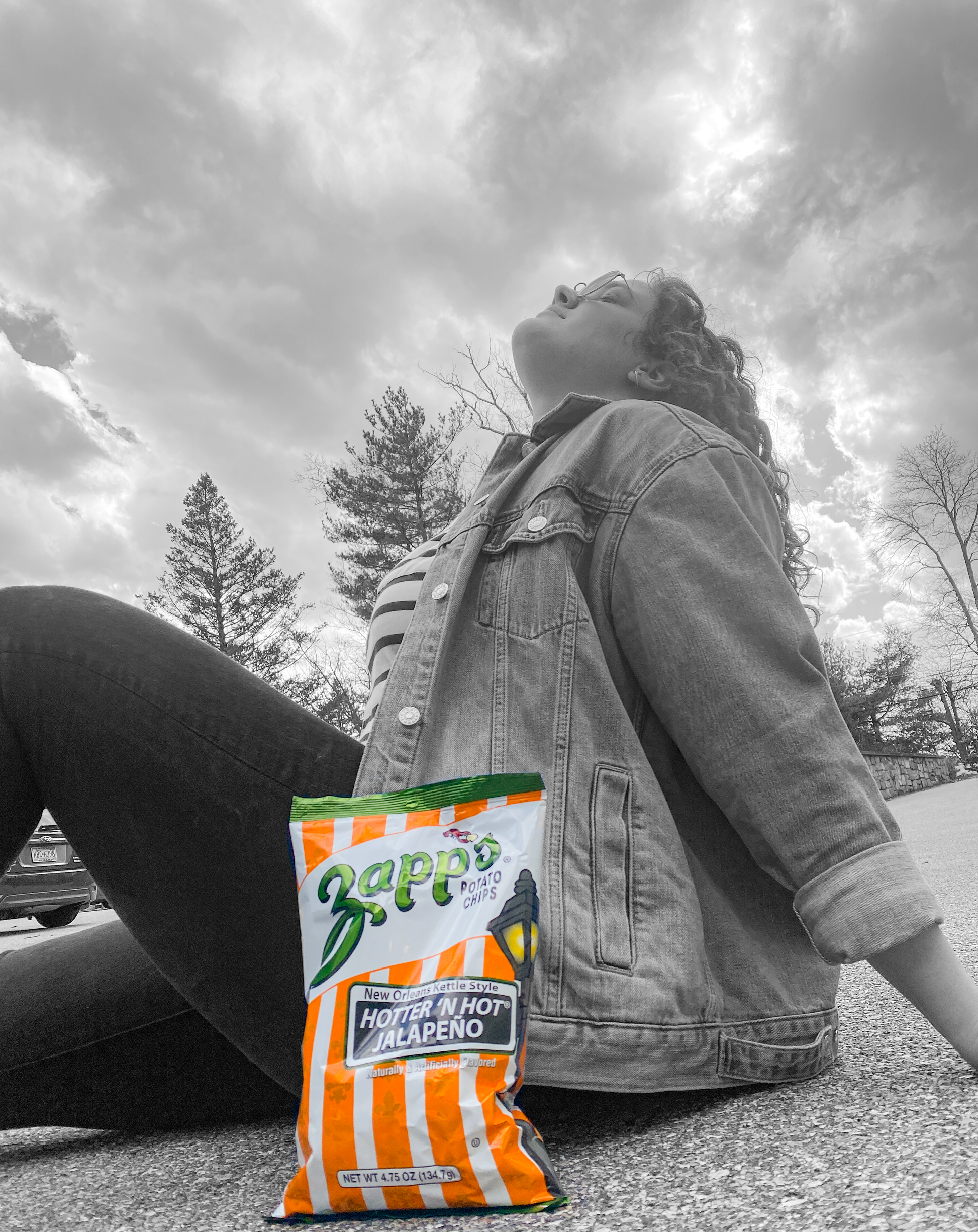 Person sitting on a road with a Zappos hot sauce packet in the foreground, against a cloudy sky.