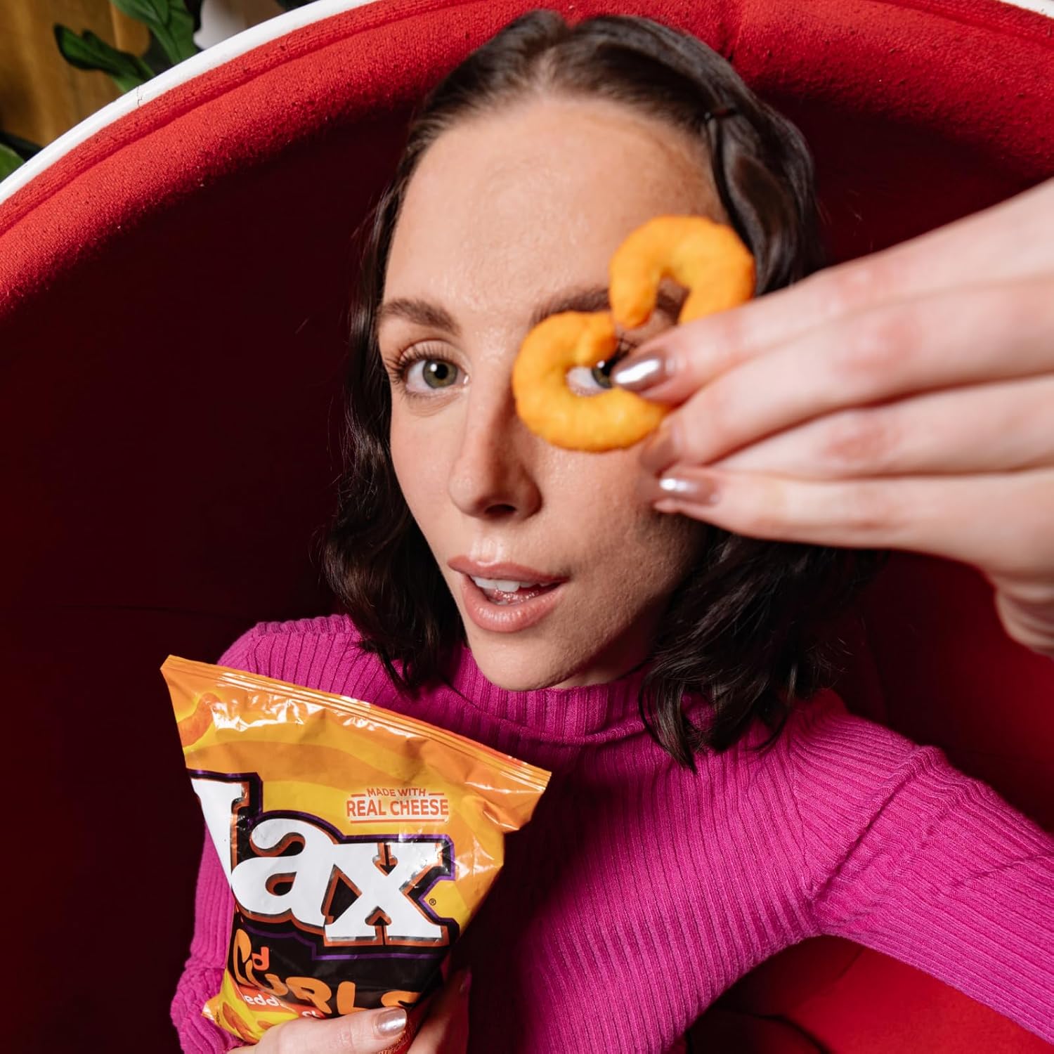 Woman holding a bag of Lays cheese puffs with a red background