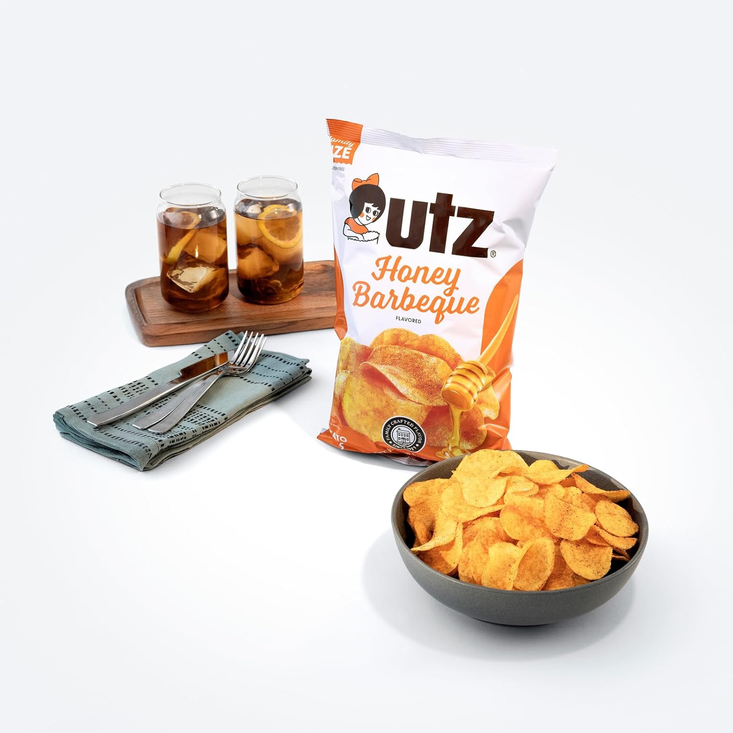 UTZ Honey Barbecue chips in a bowl with a bag of chips and drinks on a white background