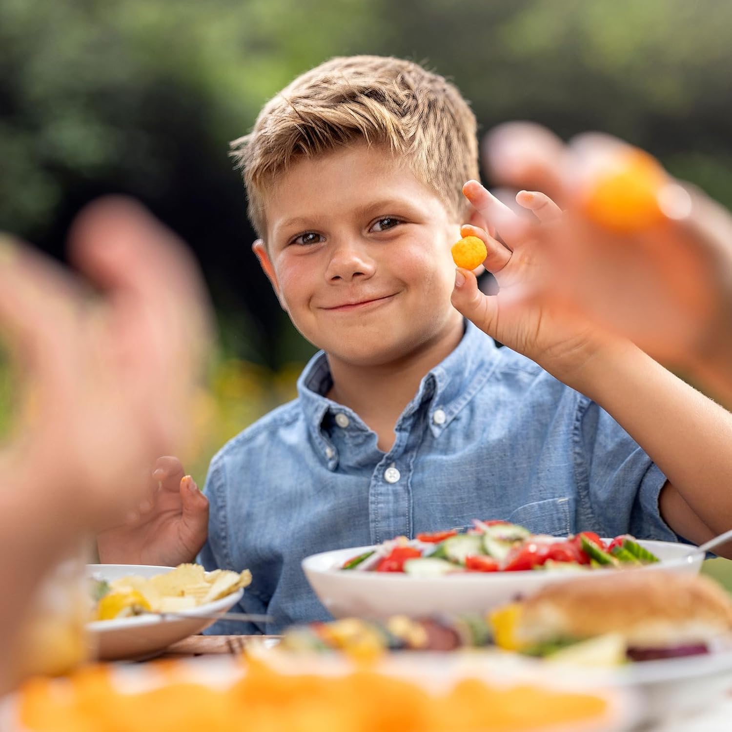 Child holding a snack outdoors with food and people in the background