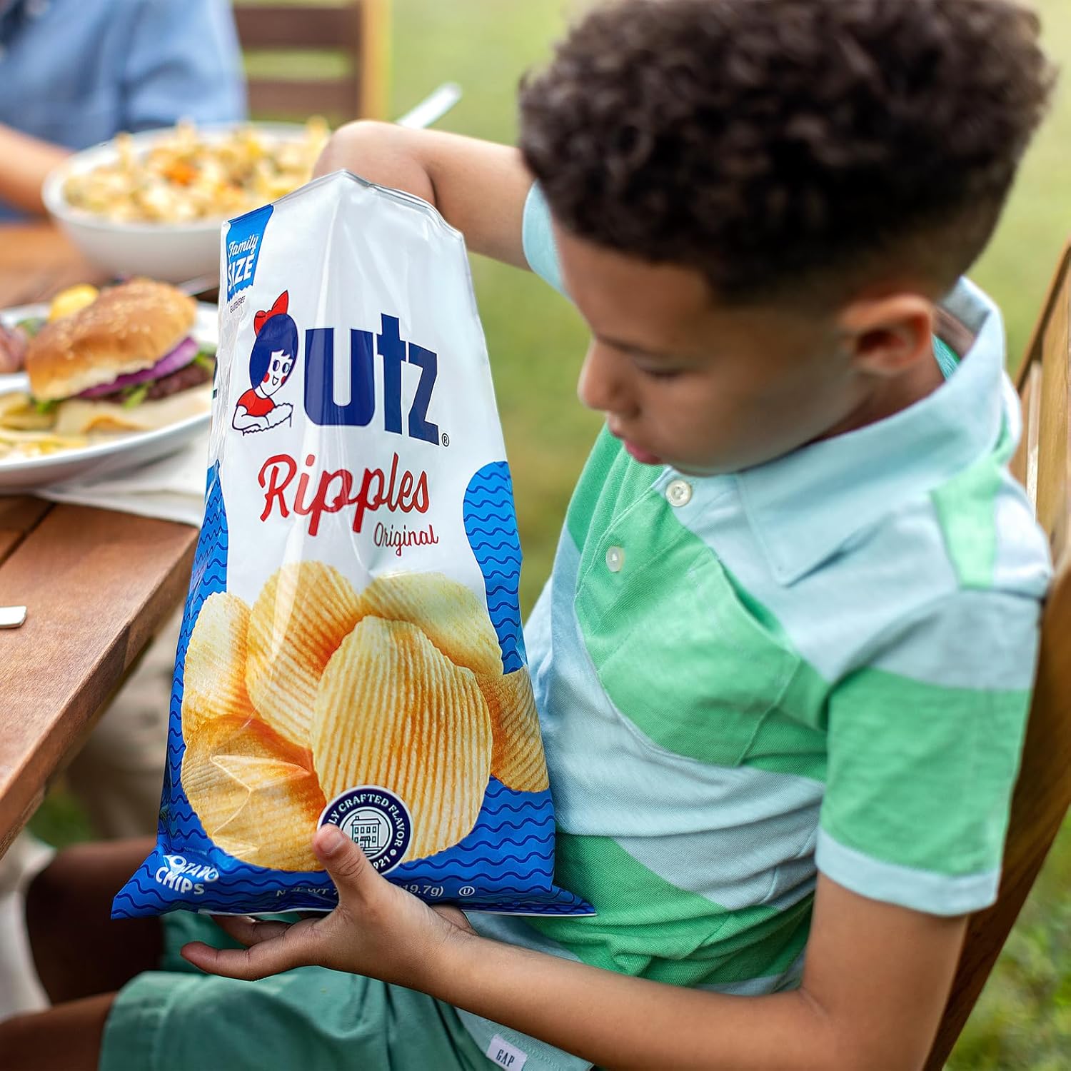 Child holding a bag of Utz Ripples potato chips outdoors