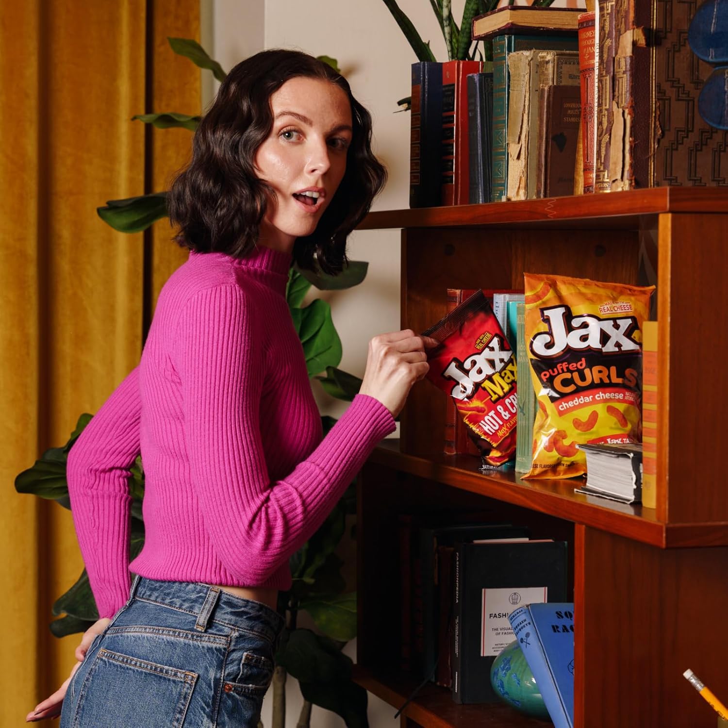 Woman in pink sweater and jeans interacting with snacks on a shelf