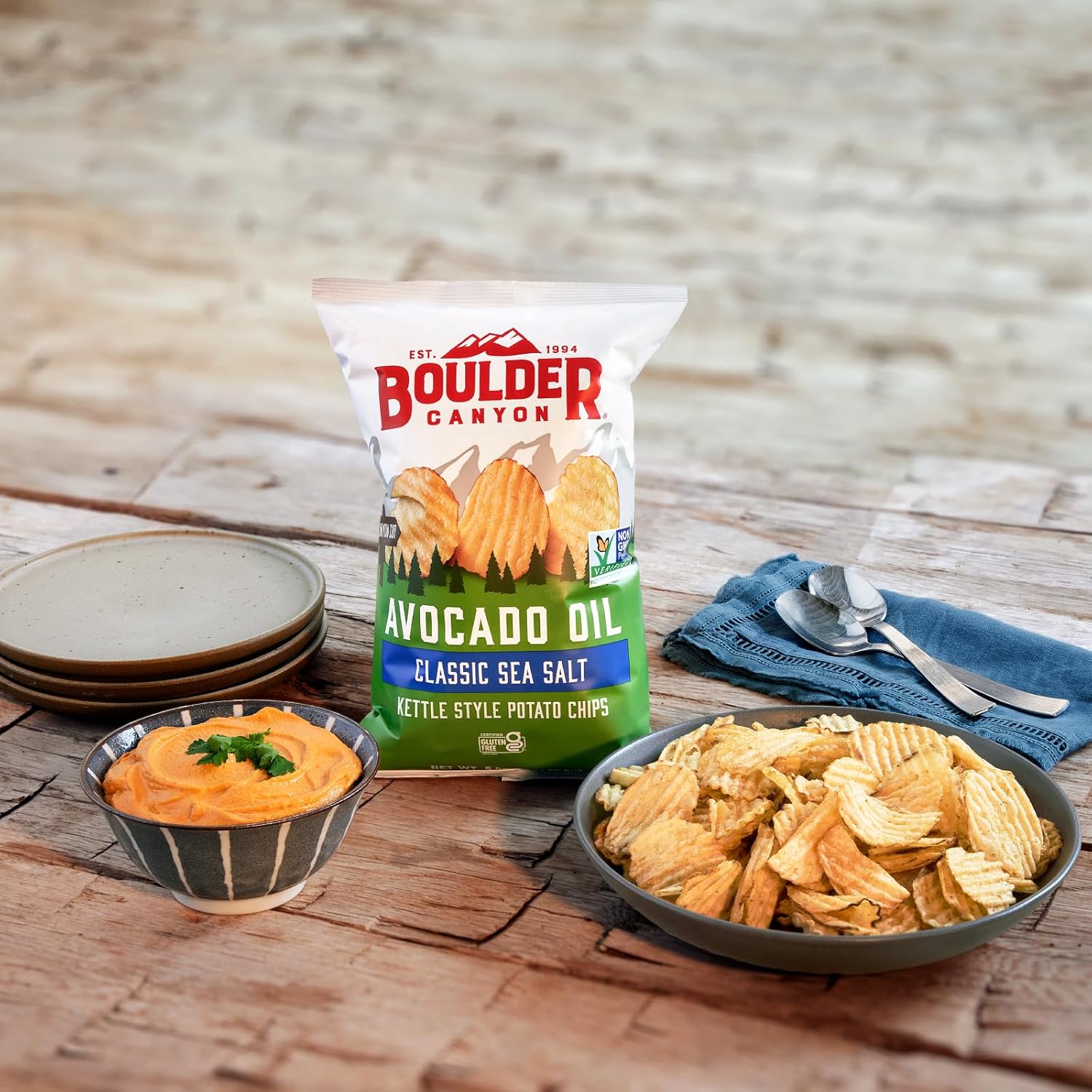Boulder Canyon avocado oil kettle style potato chips with a bowl of dip on a wooden table.