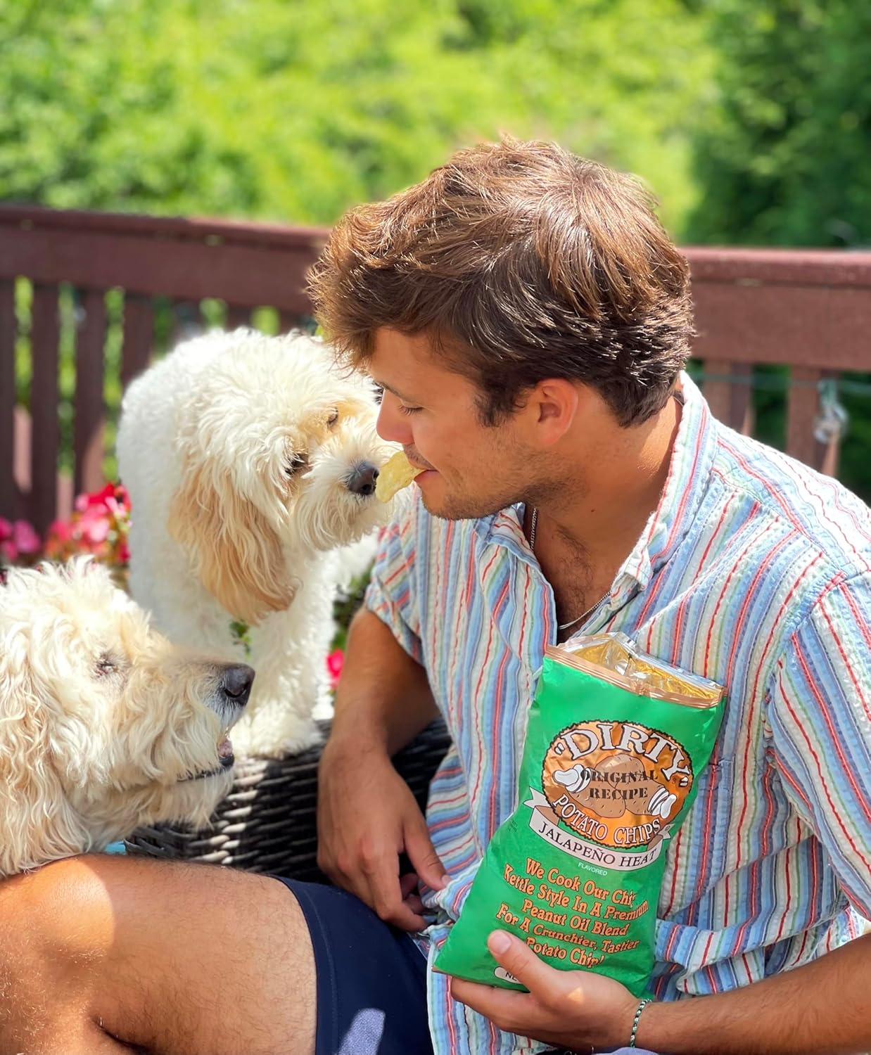 Man sitting outdoors with two dogs, holding a bag of dog food.