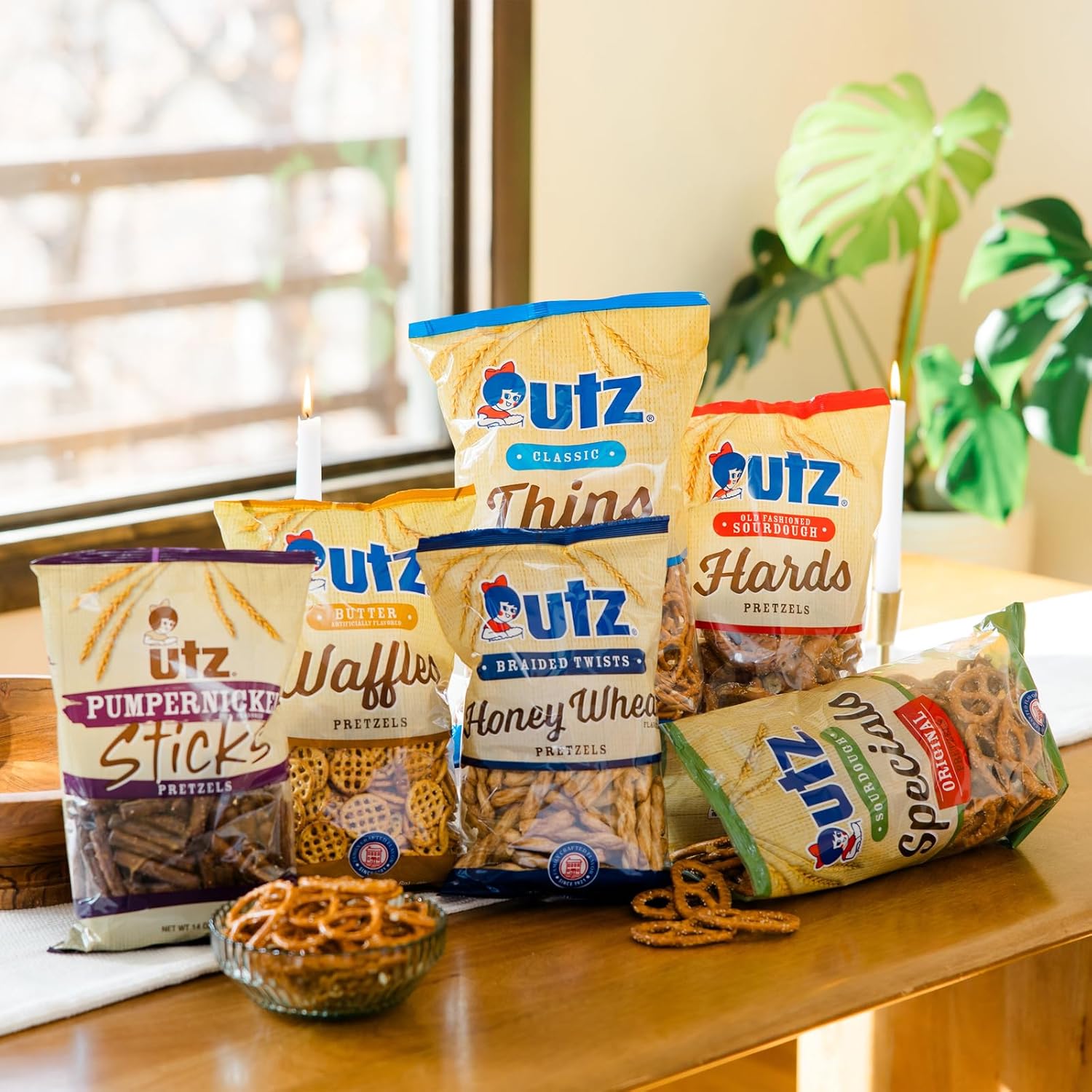 Assorted Utz pretzel products on a wooden surface with a window and plant in the background.