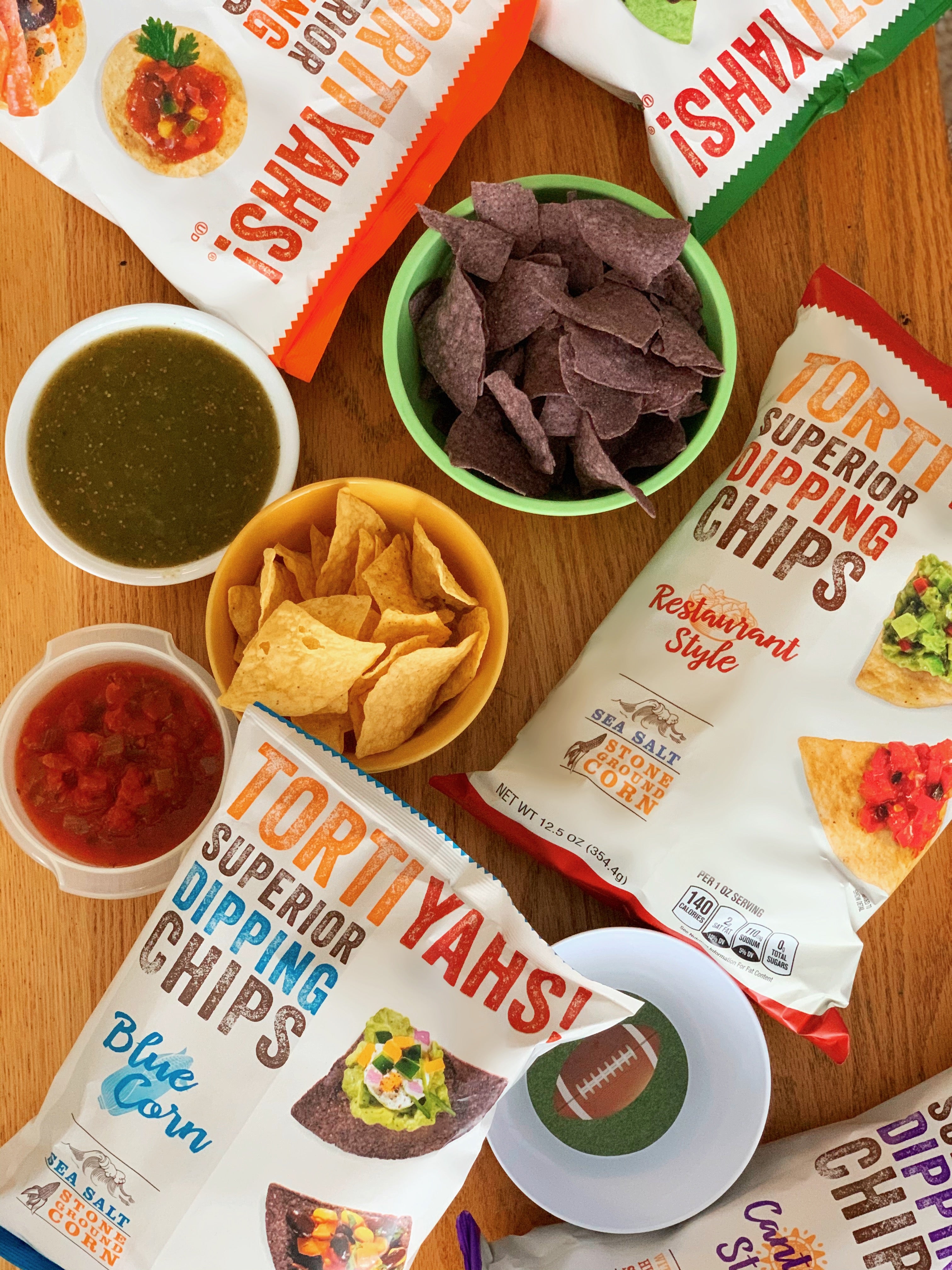 Tortilla chips and dipping sauces on a wooden table with 'Tortiyahs!' packaging.