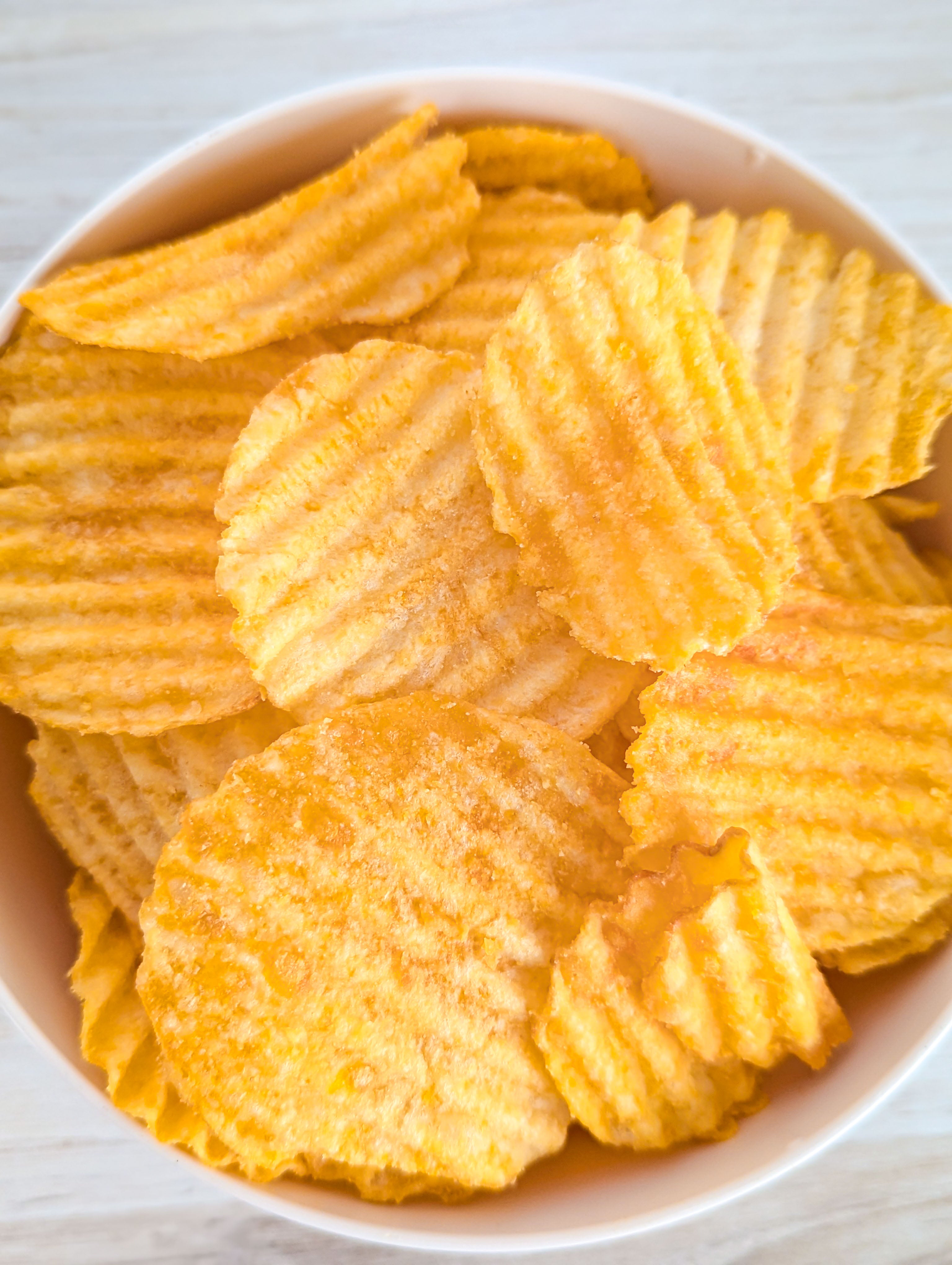 Ruffled potato chips in a white bowl on a light wooden surface