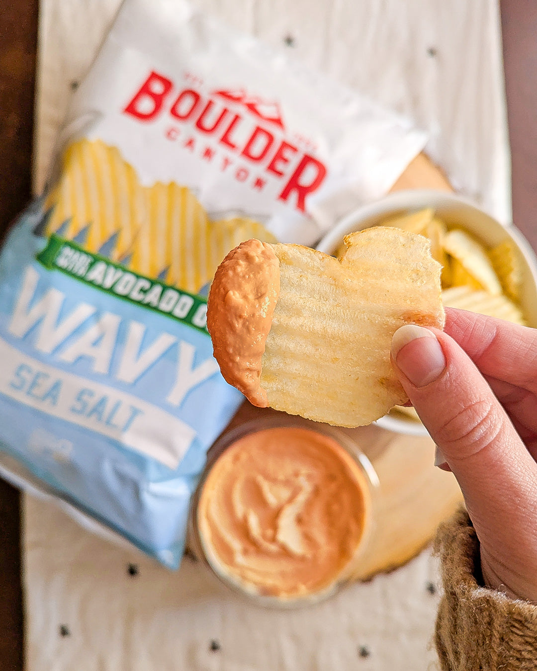 Hand holding Boulder Canyon wavy sea salt chip dipped in sauce.