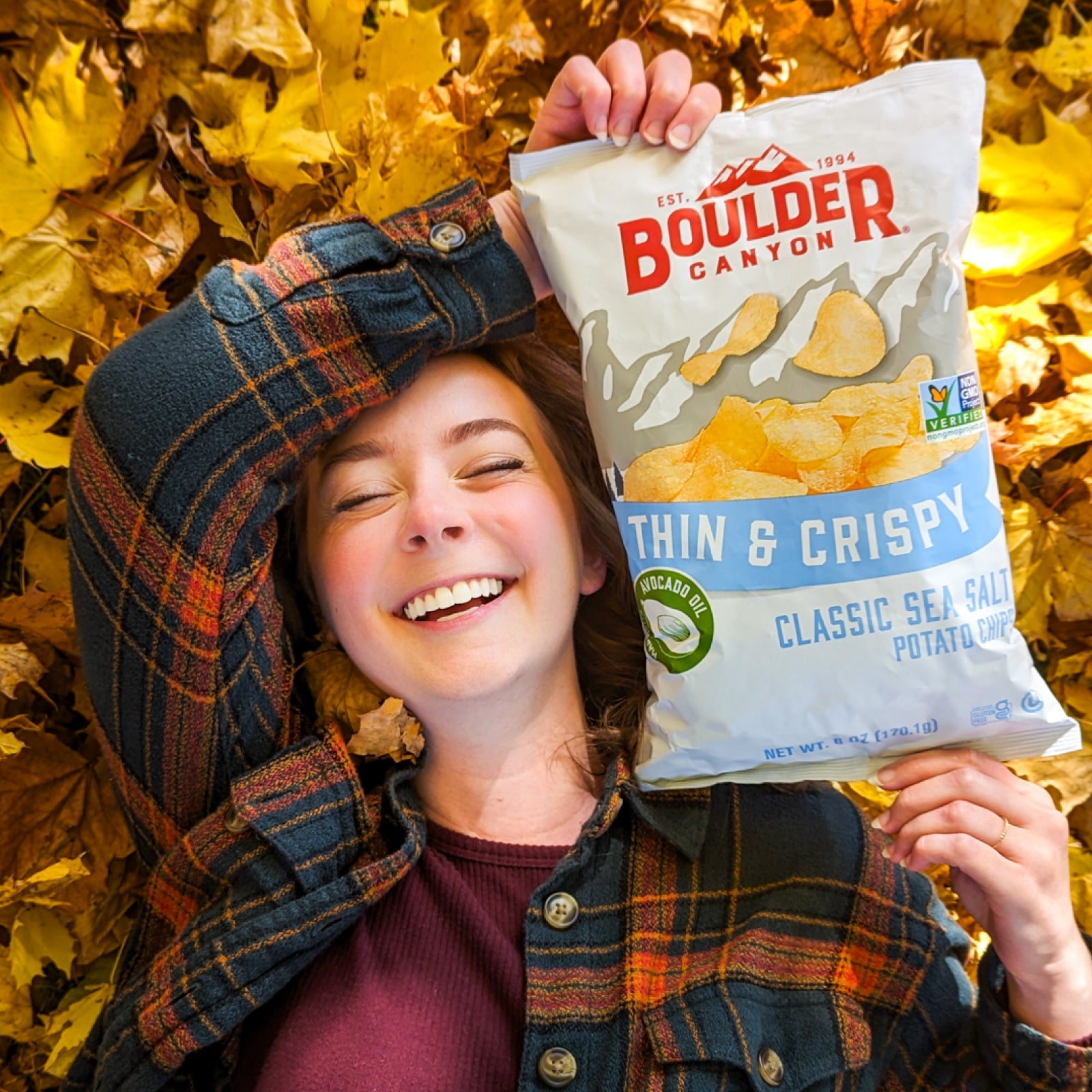 Person holding a Boulder Canyon potato chip bag among autumn leaves