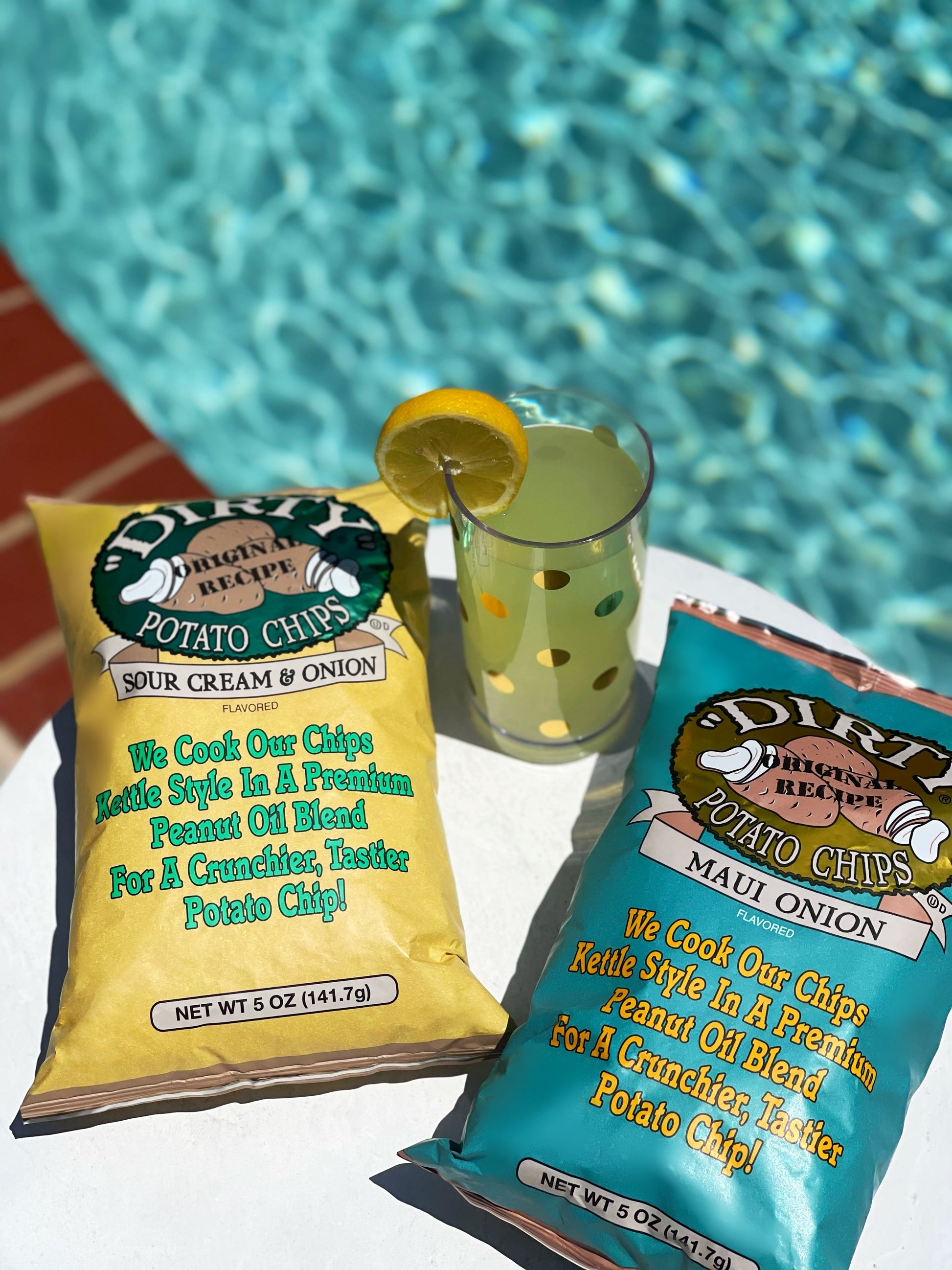 Two bags of Dirt Chips by the pool with a drink.