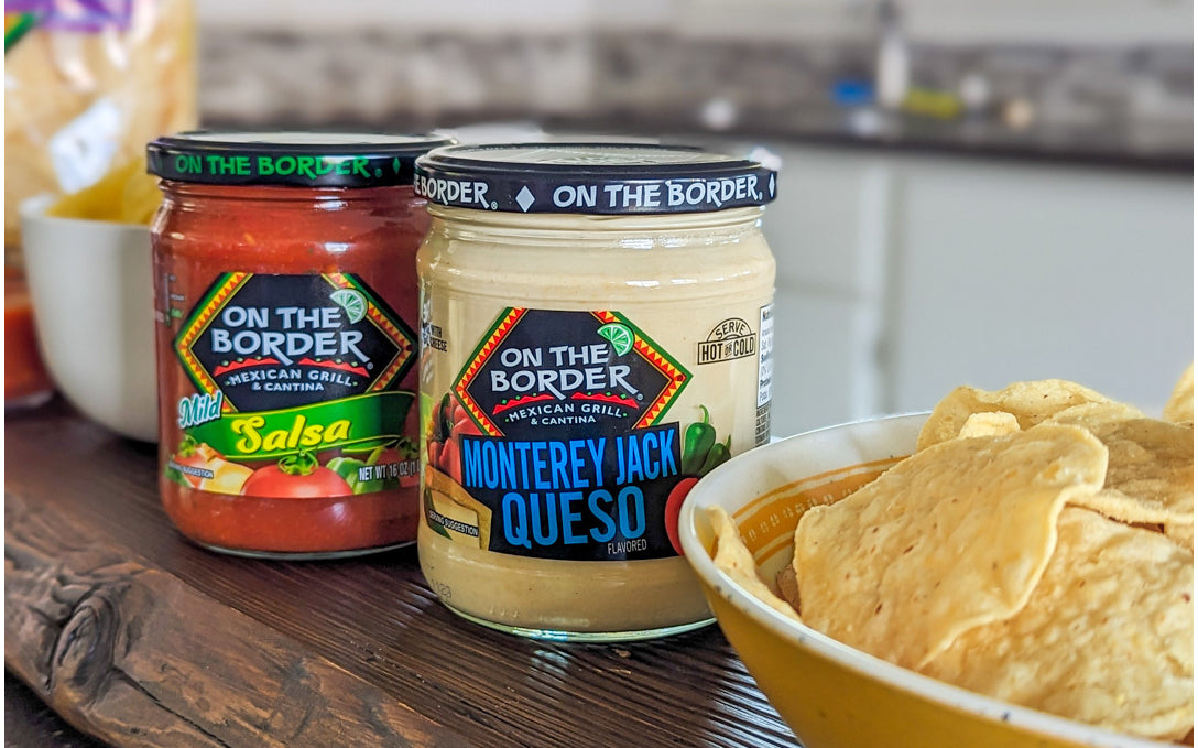 Jars of 'On the Border' salsa and queso with tortilla chips on a wooden surface.