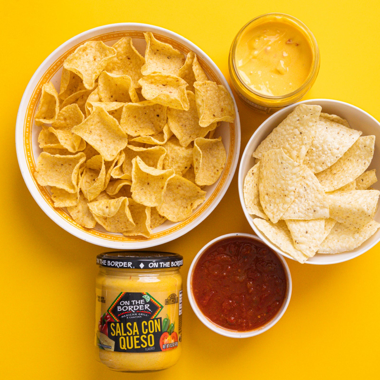 Tortilla chips with salsa and a jar of salsa on a yellow background