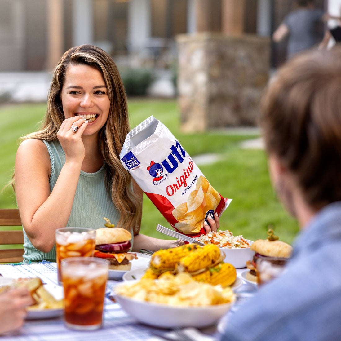 Woman eating chips at a picnic table with friends, Utz Originals bag visible
