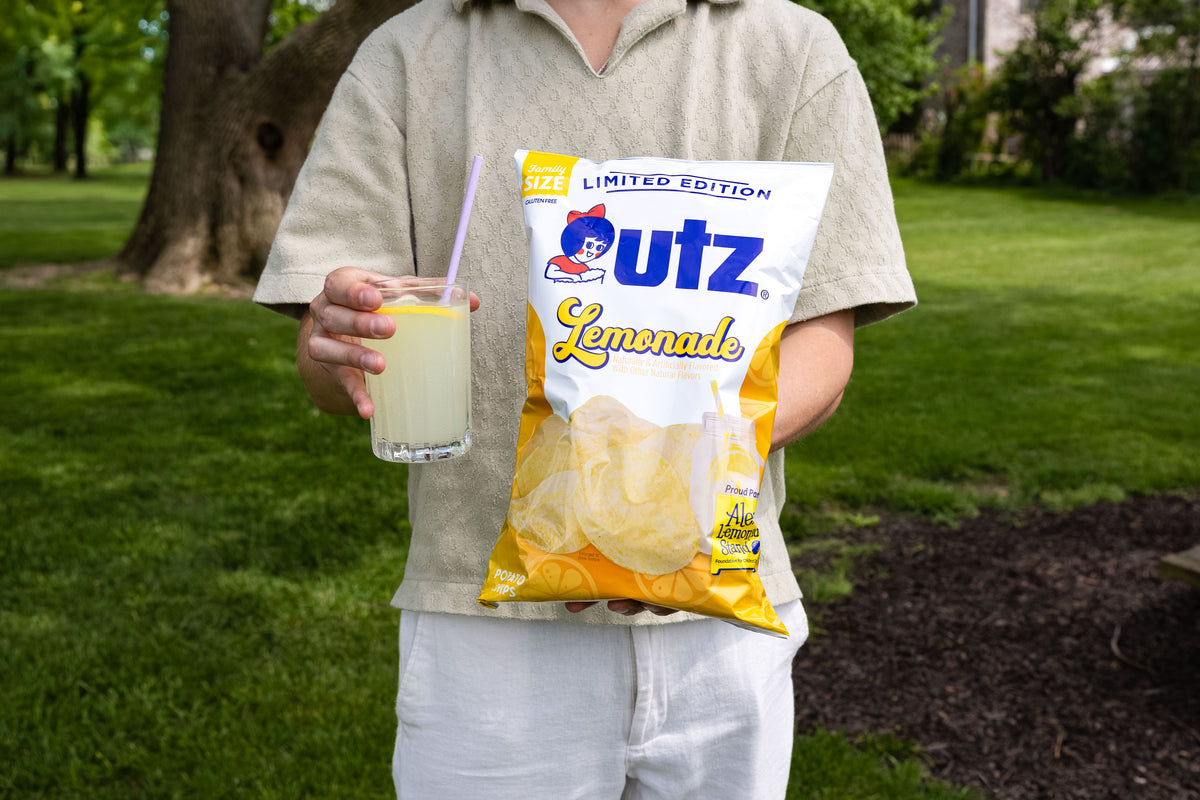 Person holding a Outz Lemonade package and a drink outdoors.