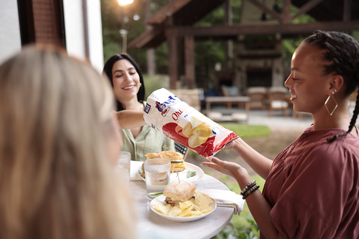 Woman holding a bag of Lay's potato chips at an outdoor gathering.