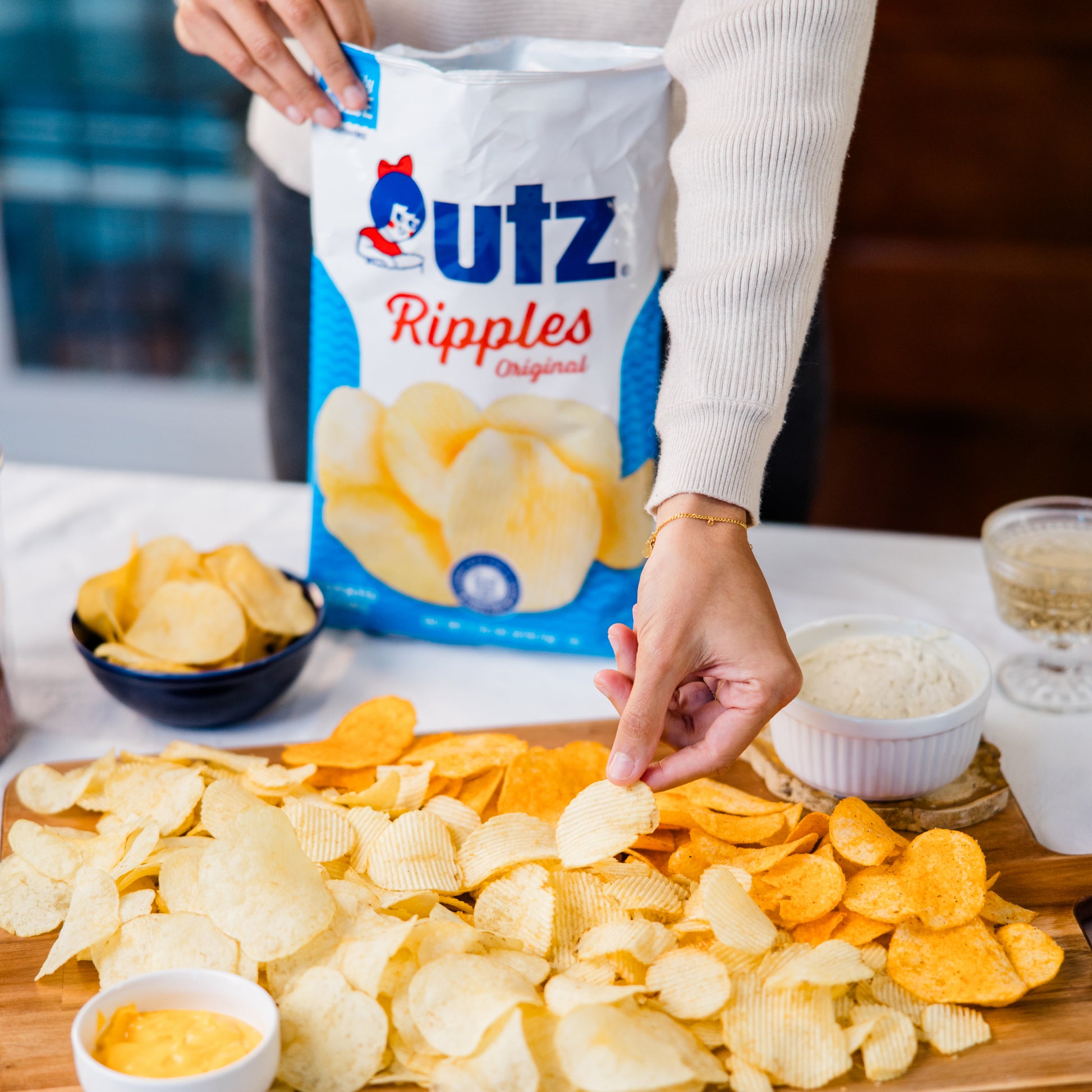 Person reaching for Utz Ripples Original potato chips on a table with a bag of chips in the background.