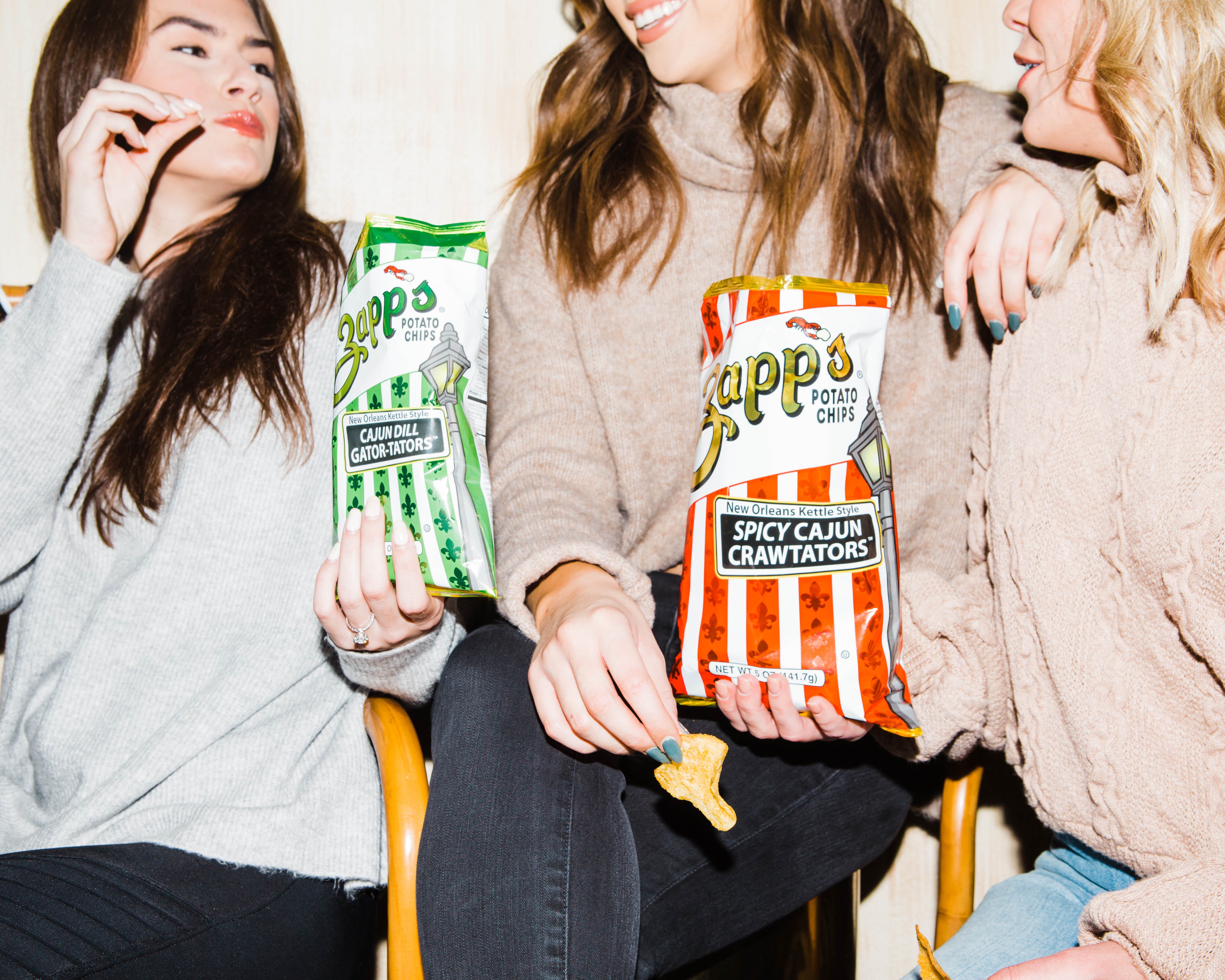 Three people sitting together holding Zappo's snack packets.