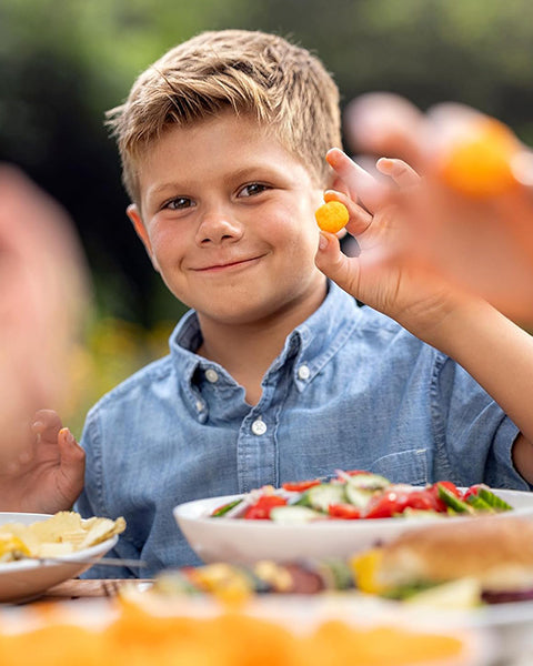Child holding a piece of food outdoors with a plate of salad in front